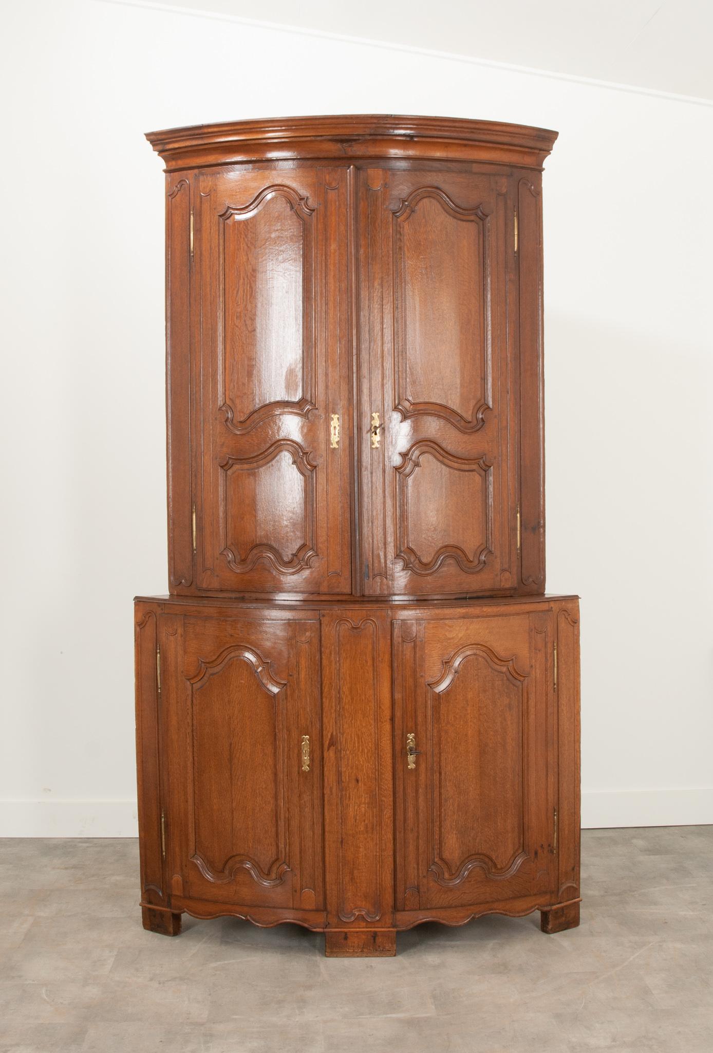 This substantial corner buffet a deux corps was made in 19th century France from solid walnut. The top portion is crowned with a molded cornice over rounded double doors with shapely carved panels. Unlocking the solid doors reveals two fixed