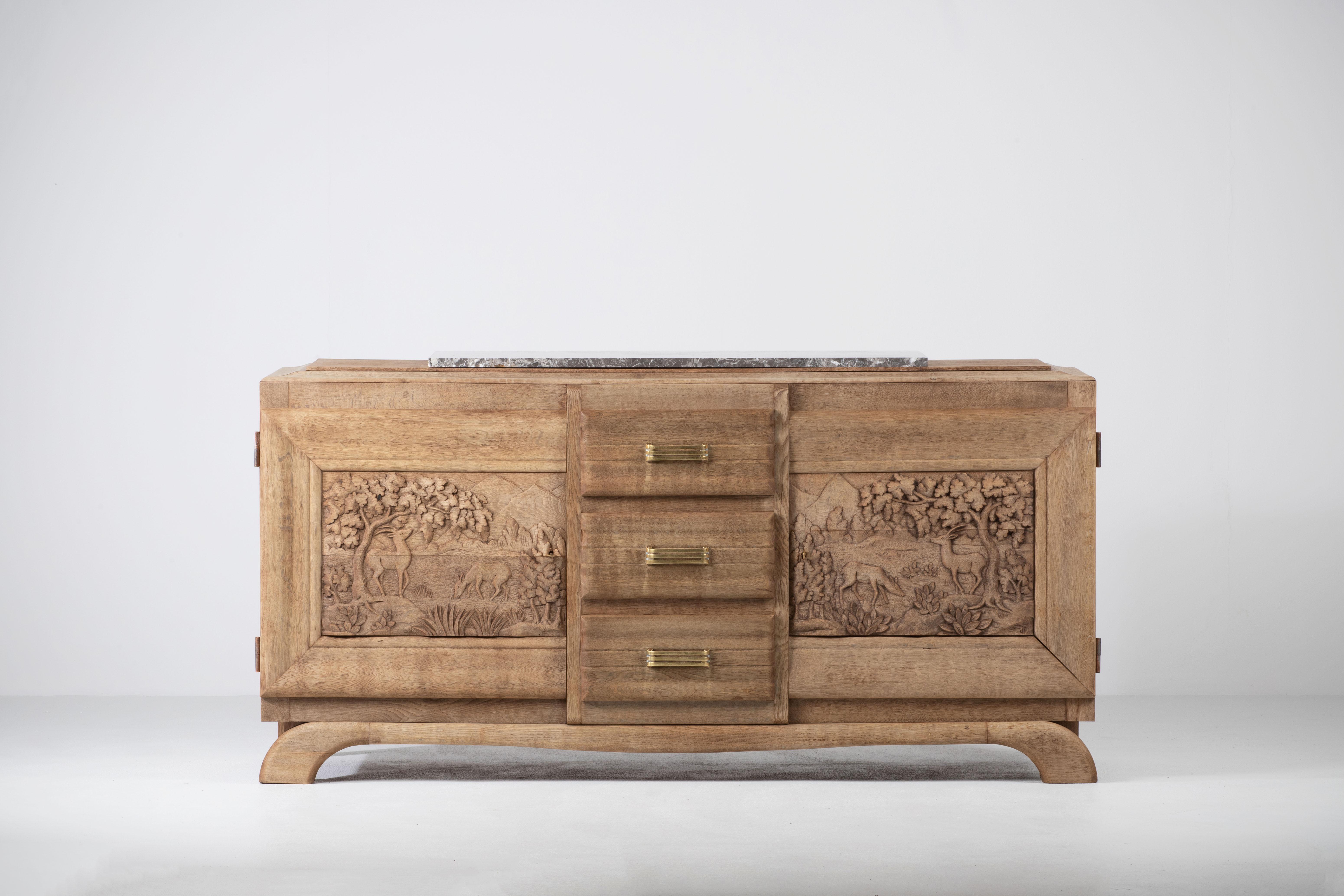 Very elegant credenza in solid oak, France, 1940s.
Art Deco Brutalist sideboard. 
The credenza consists of Two storage facilities covered with handcarved hunting scene designed doors and a column of drawers.
The refined wooden structures on the