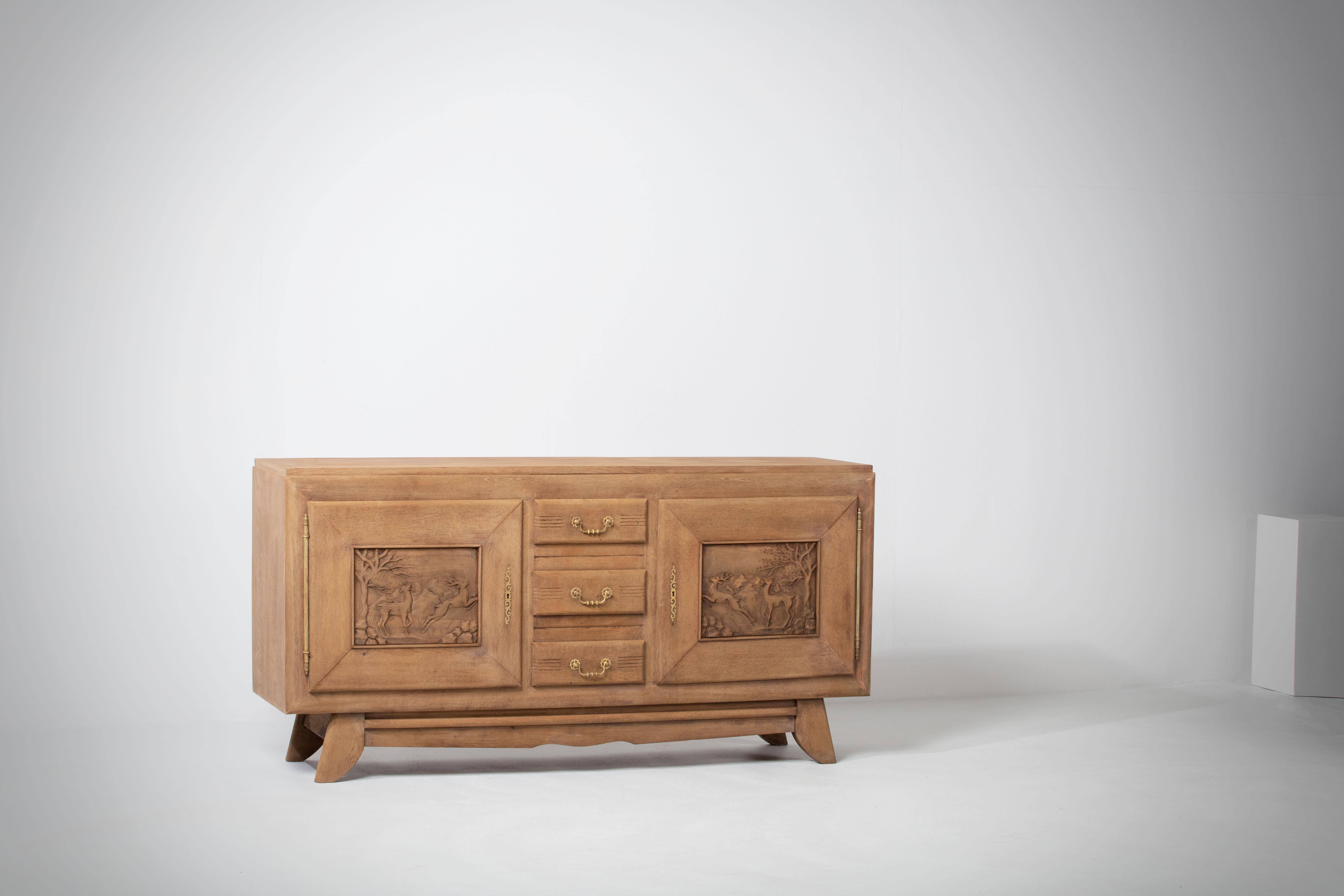 Very elegant credenza in solid oak, France, 1940s.
Art Deco Brutalist sideboard. 
The credenza consists of Two storage facilities covered with handcarved hunting scene designed doors and a column of drawers.
The refined wooden structures on the