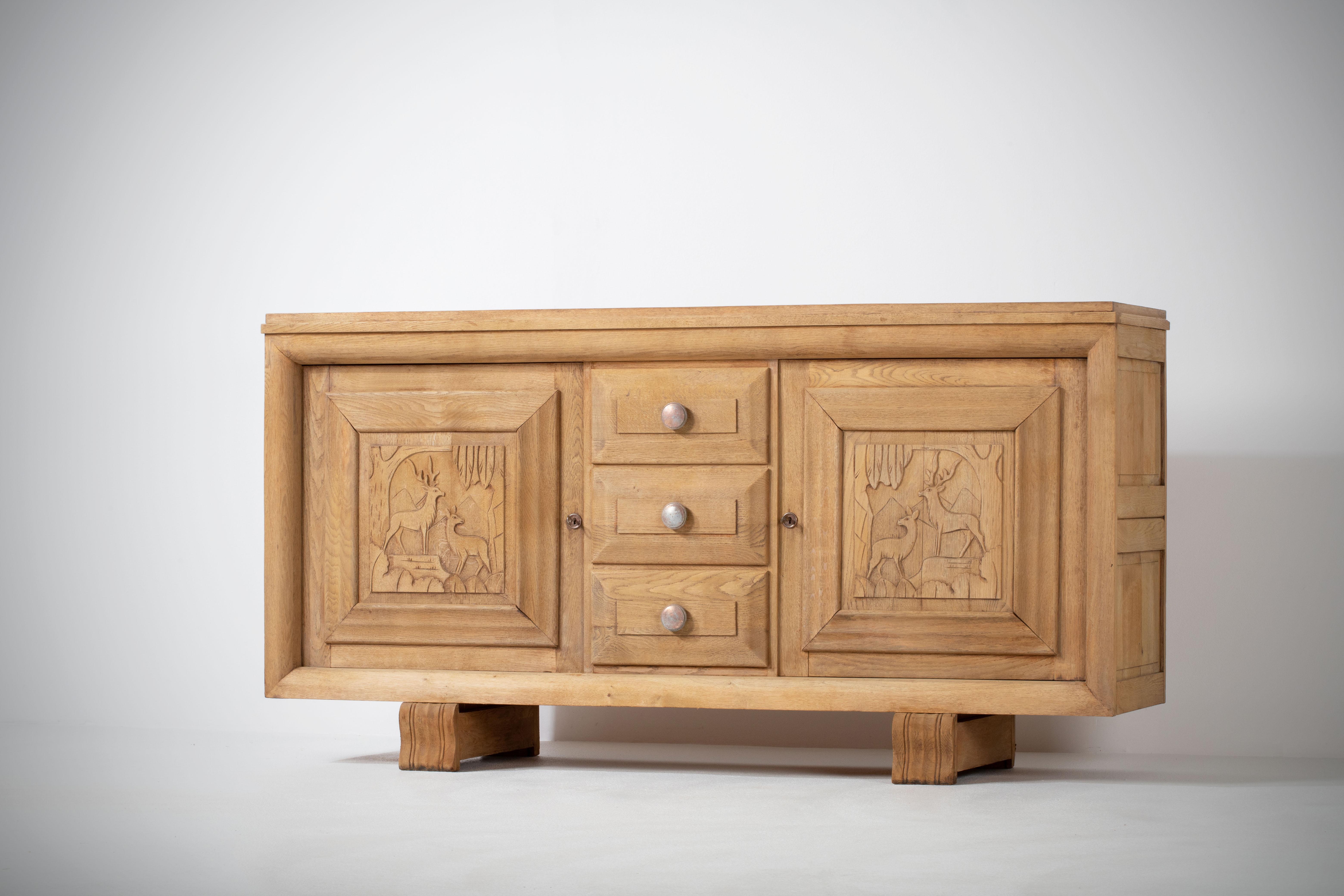 Very elegant credenza in solid oak, France, 1940s.
Art Deco brutalist sideboard. 
The credenza consists of two storage facilities covered with handcarved hunting scene designed doors and a column of drawers.
The refined wooden structures on the