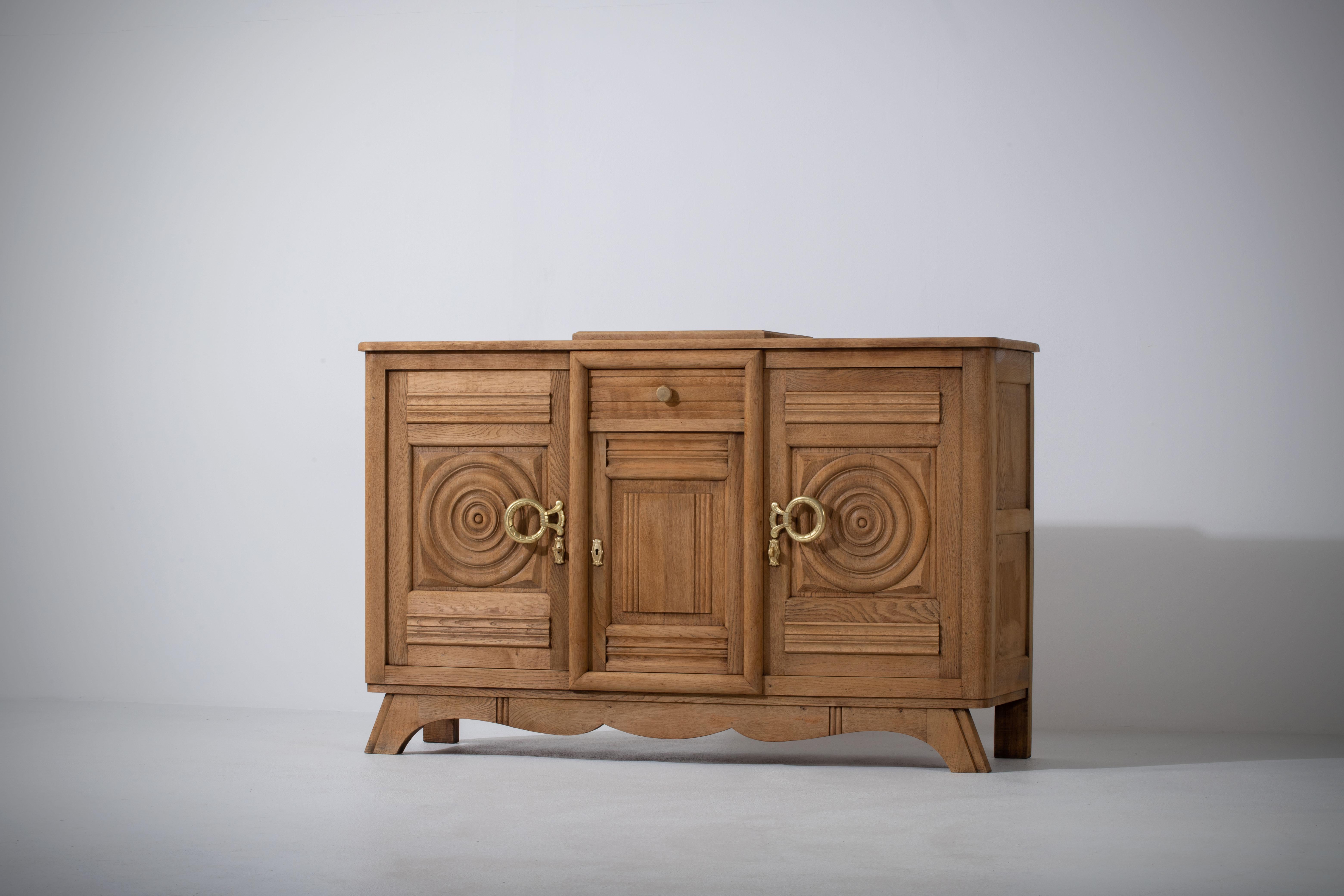 Very elegant credenza in solid oak, France, 1940s.
Art Deco Brutalist sideboard. 
The credenza consists of two storage facilities covered with hand carved designed doors and a drawers and cocktail cabinet.
The refined wooden structures on the