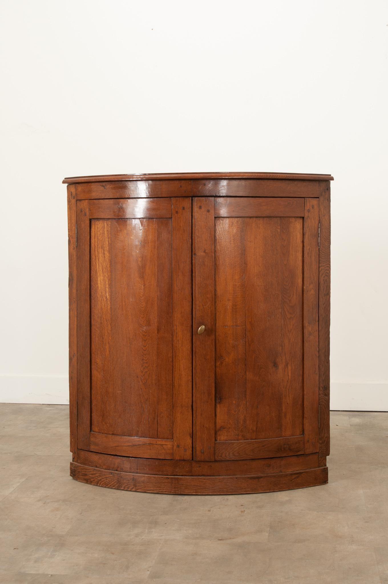 A sleek and simple French solid oak corner cabinet that will add a bit more storage space without taking up too much room. Hand-crafted in the 19th century, its polished demilune top showcases the rich tones and patina of the oak. The body is curved