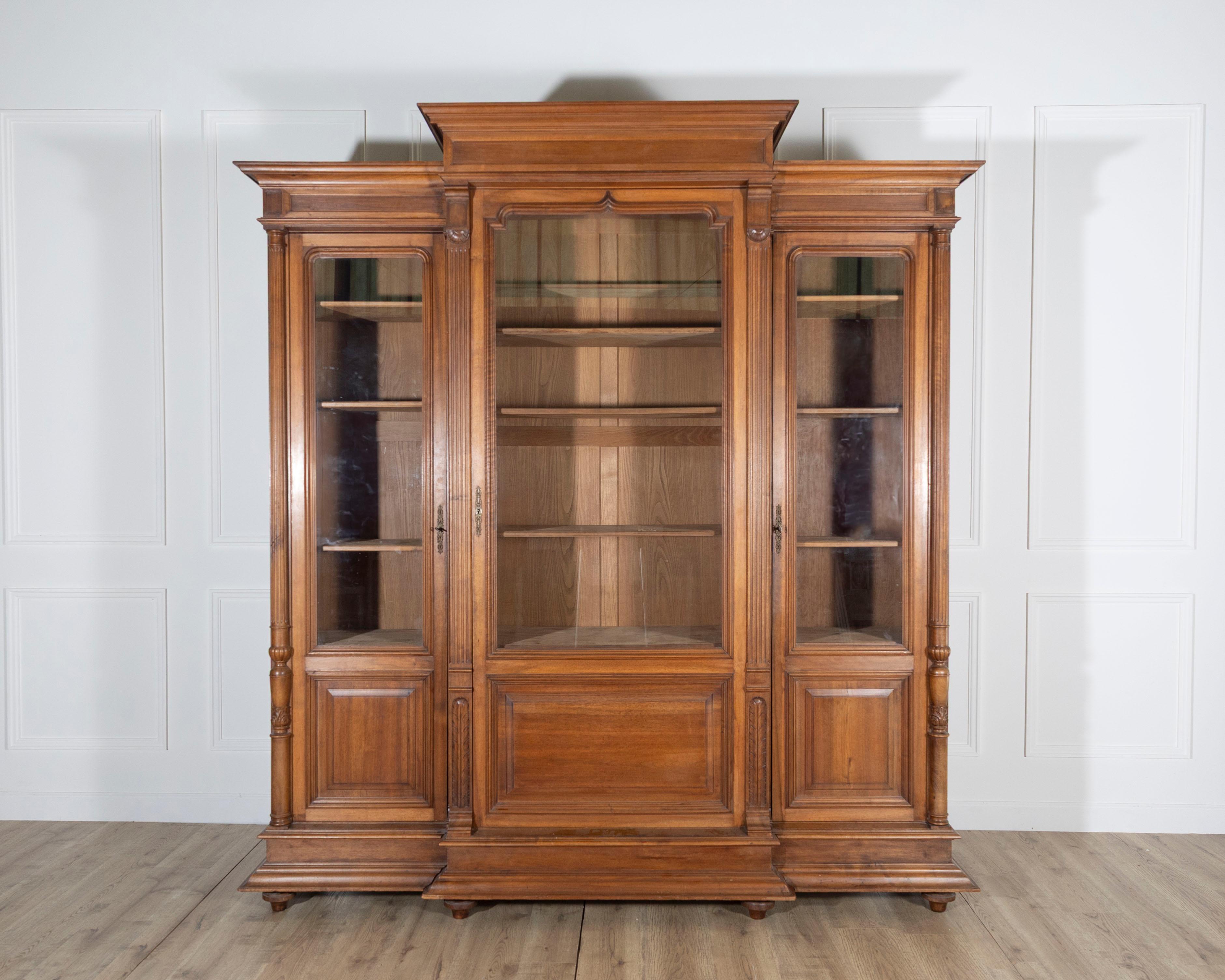 A grand French bookcase in solid walnut, dating to the late 19th century, showcasing both elegance and durability. The architectural form is accentuated by detached columns carved with vertical grooves and acanthus leaf capitals, lending a classical