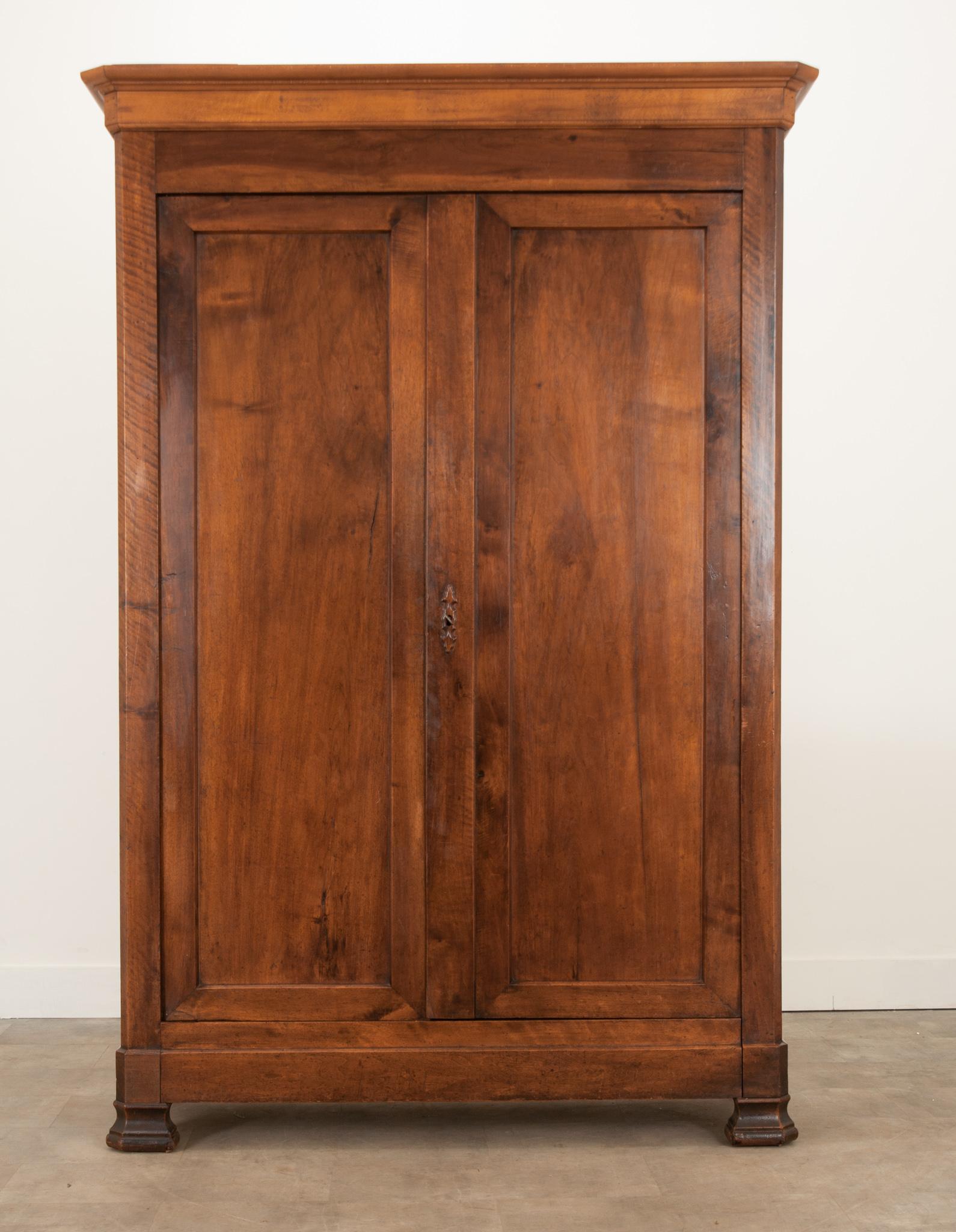 A refined armoire built in France during the 1830’s from solid walnut, in the style of Louis Philippe. A carved escutcheon plate graces the paneled doors, which unlock to reveal a nicely sized storage cavity. One fixed key is included. Three