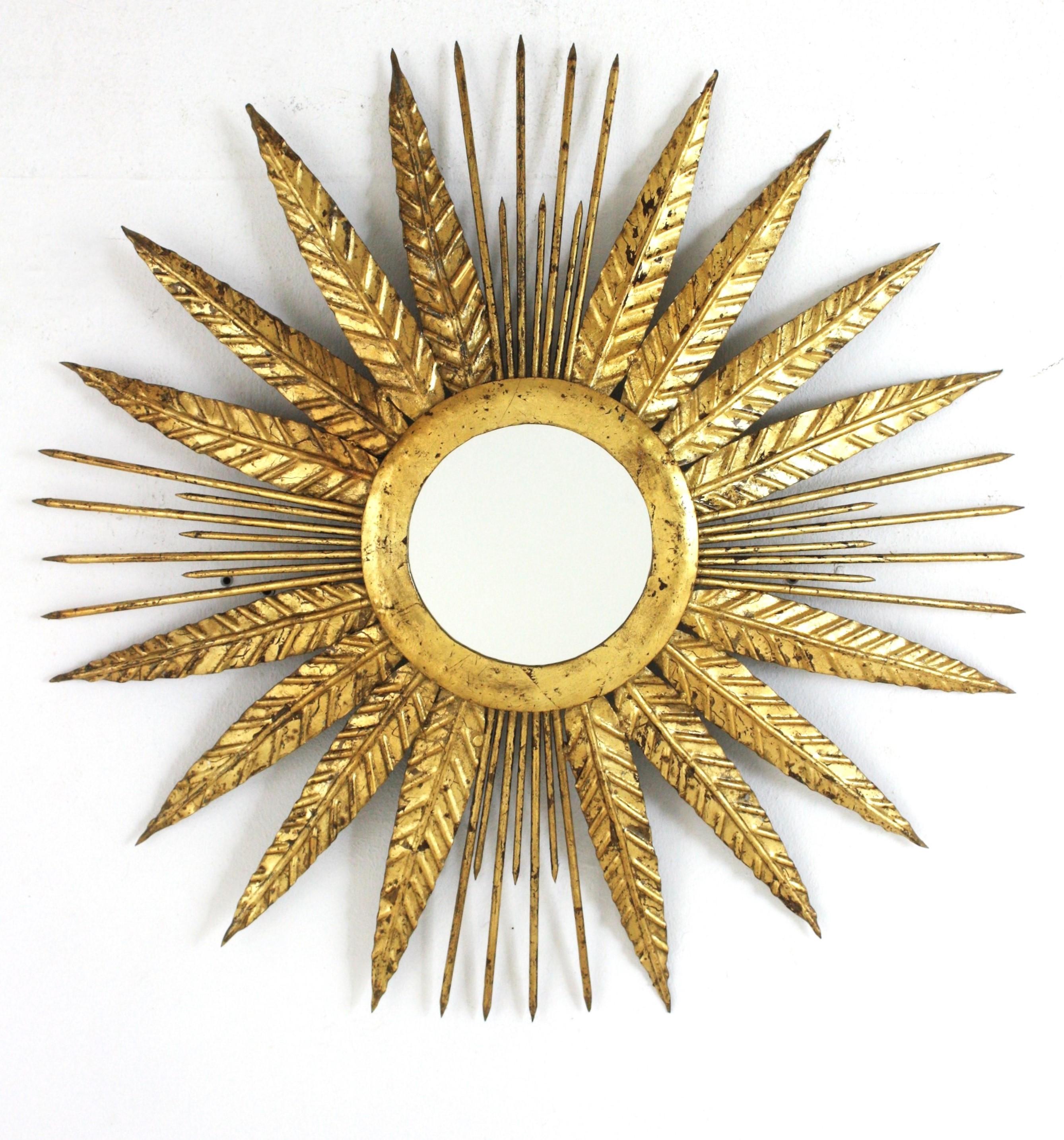 French sunburst mirror in gilt iron with leaves and  spikey gilt nail rays. France, 1940s.
Eye-catching hand-hammered gold leaf gilt iron leafed sunburst mirror from the late Art Deco period.
Highly decorative design alternating four iron leaves