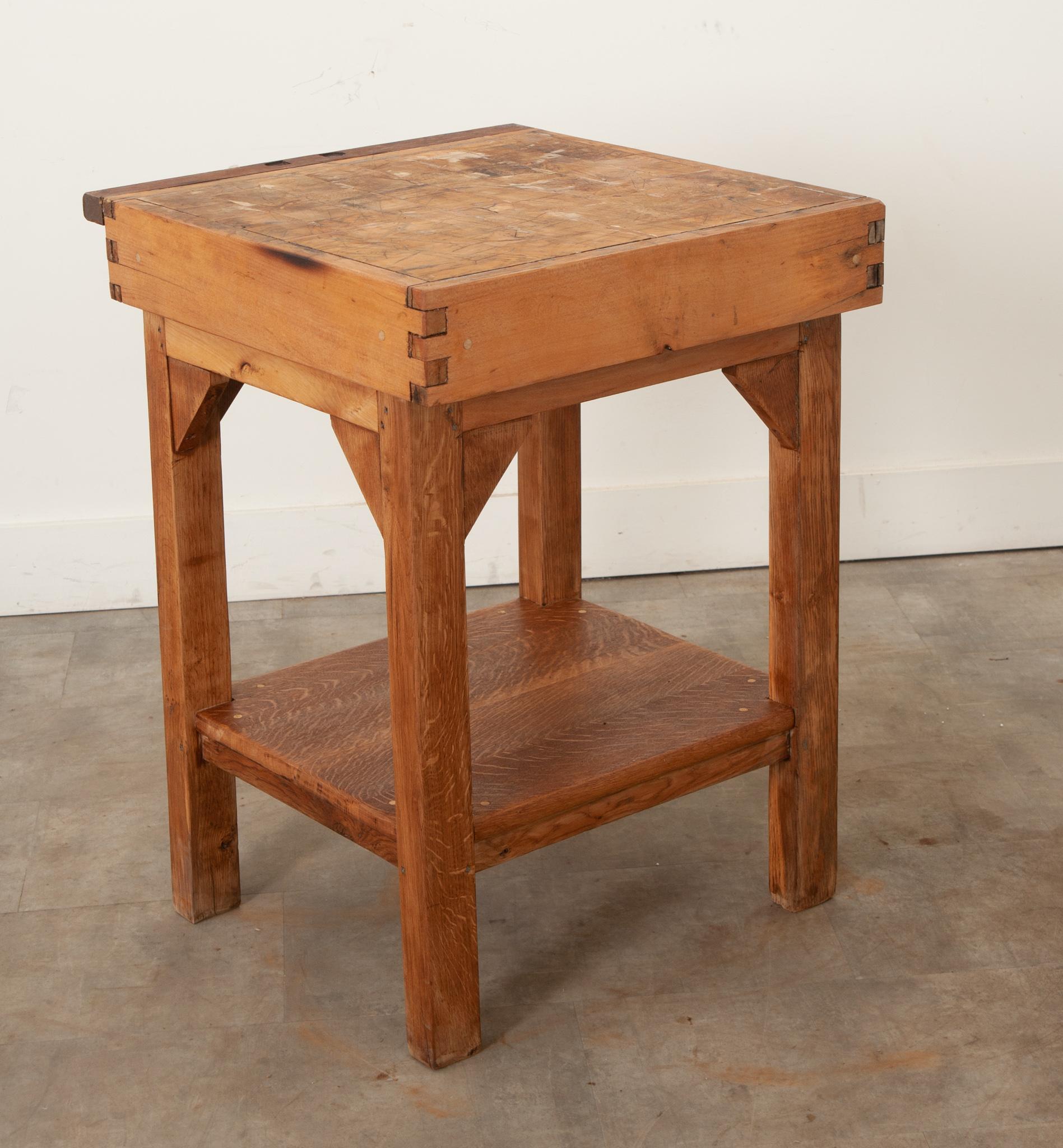 A French hand-carved square butcher block table made from oak and pine. This functional antique has a thick top made of many wood fragments all held together with steel bindings. The blocky legs are joined by a stretcher shelf below. The entire