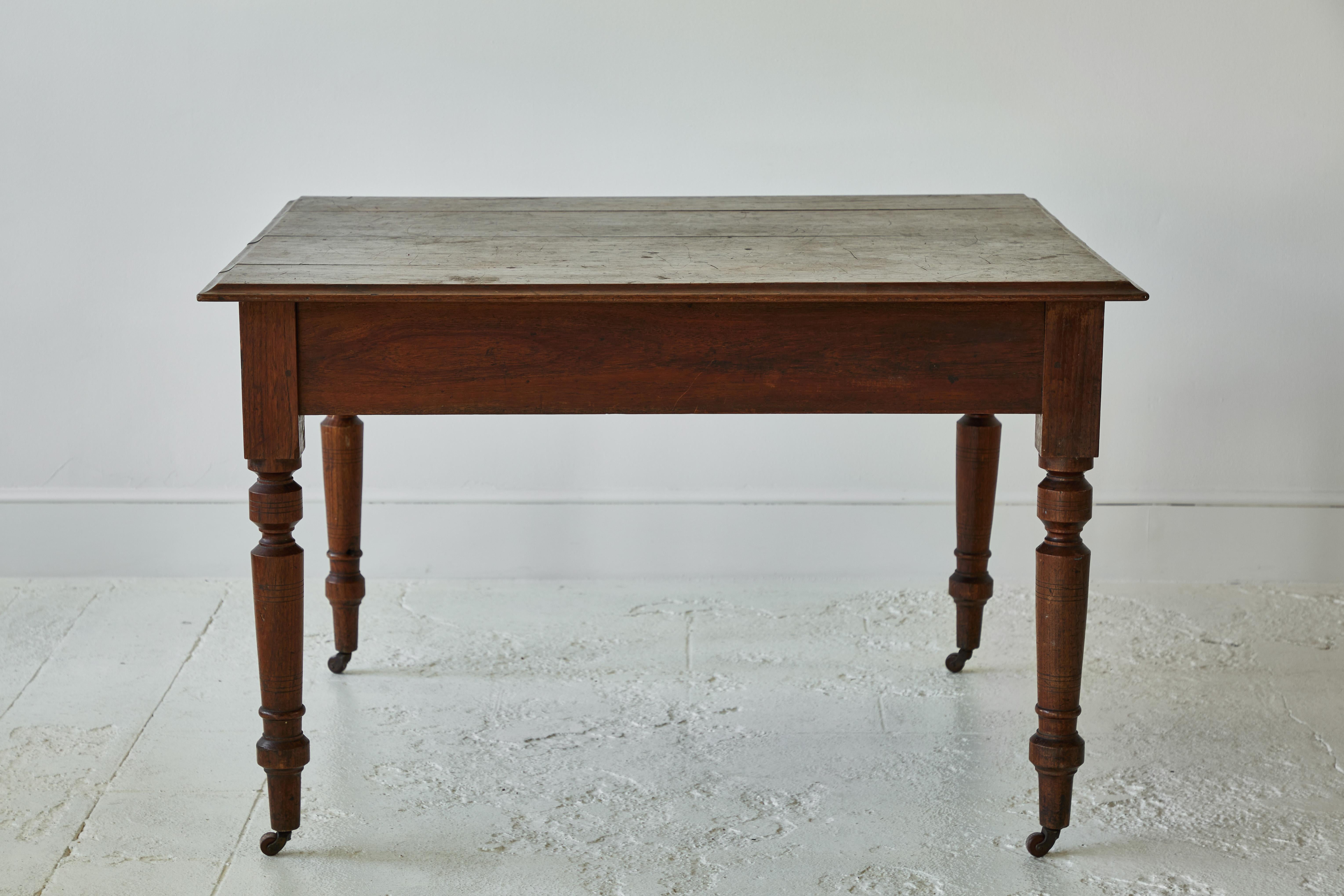 French square dark stained table with turned legs on casters.