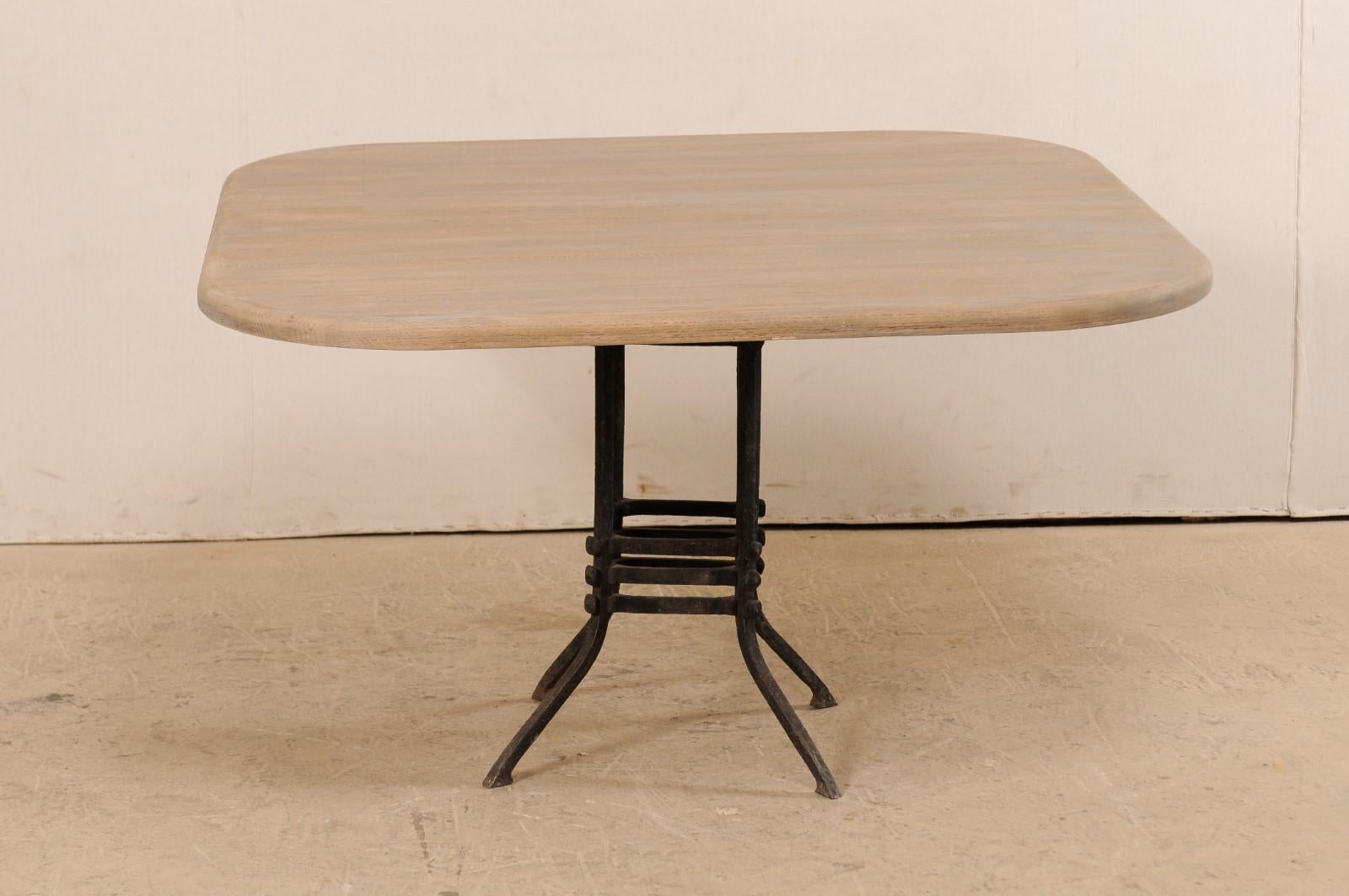A French square-shaped wood top table with 19th century iron base. This custom table has been fashioned with a reclaimed wood top, which is square in shape with rounded corners, which is raised upon a 19th century French black iron base. The base