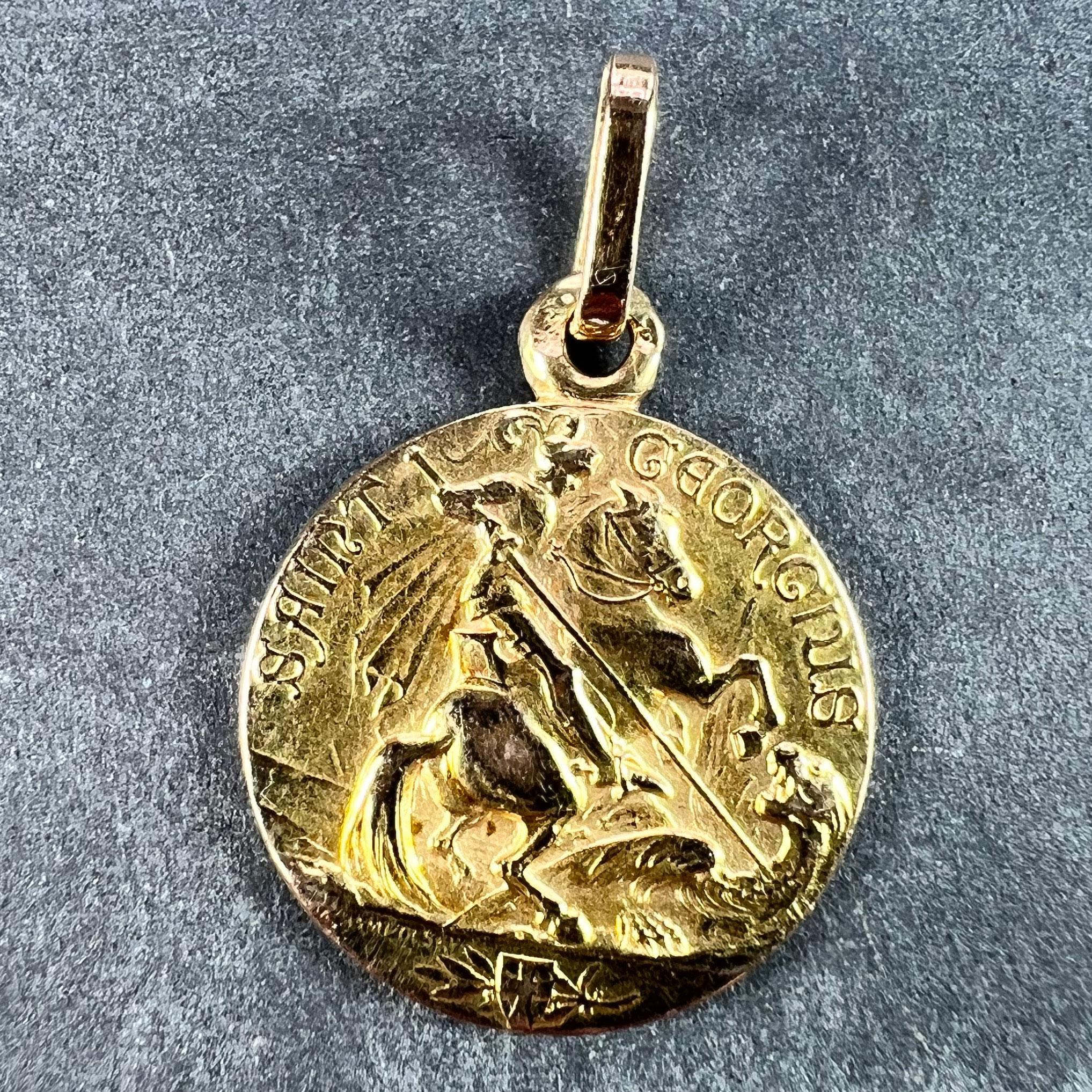 A French 18 karat (18K) yellow gold charm pendant designed as a medal depicting St George on a rearing horse defeating the dragon above a shield depicting the St George Cross with a laurel brance for victory. The phrase Saint George written above.