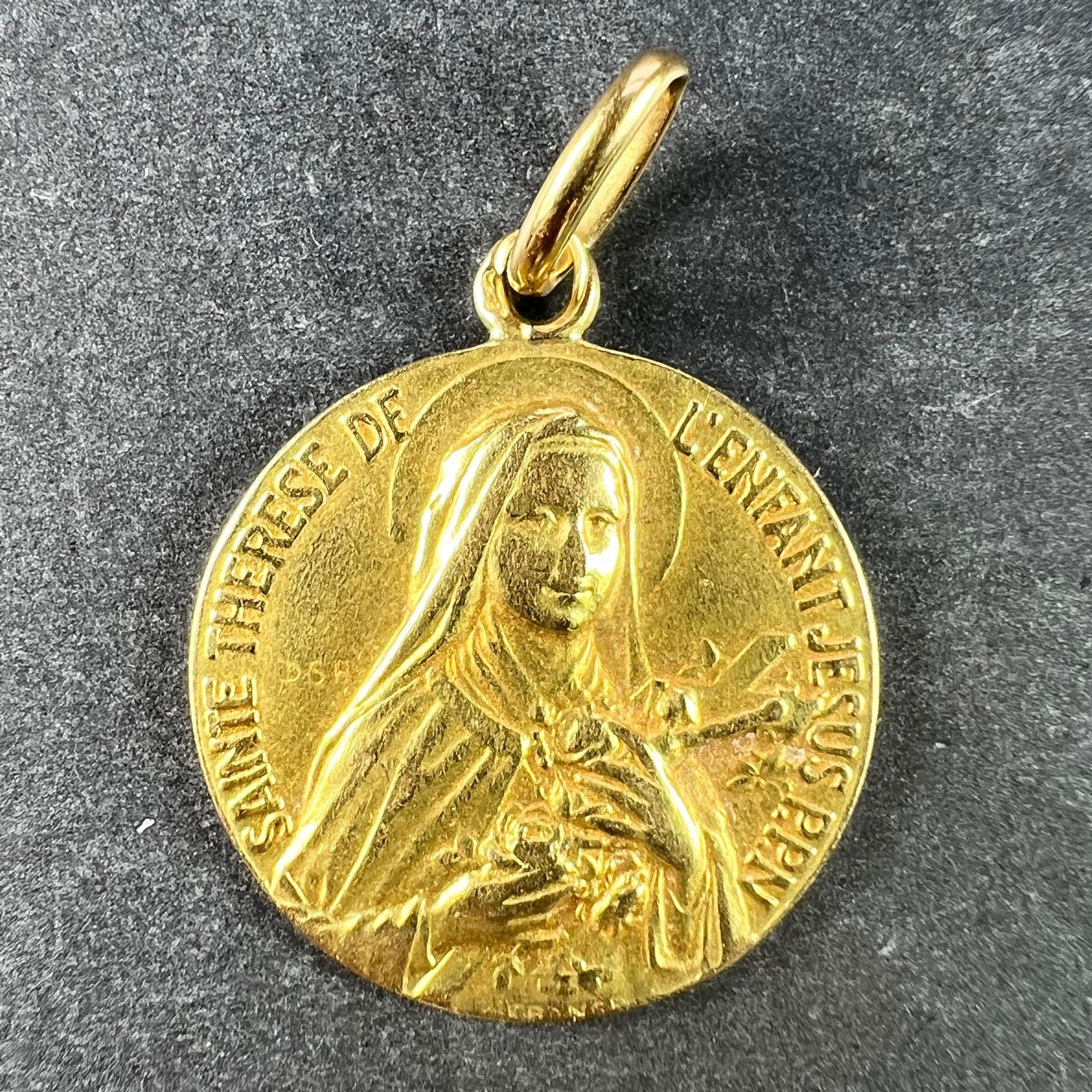 A French 18 karat (18K) yellow gold charm pendant designed as a religious medal depicting Saint Therese with the motto 'SAINTE THERESE DE L'ENFANT JESUS PPN'. St Therese is shown holding flowers and a crucifix; and was known as 'The little flower of