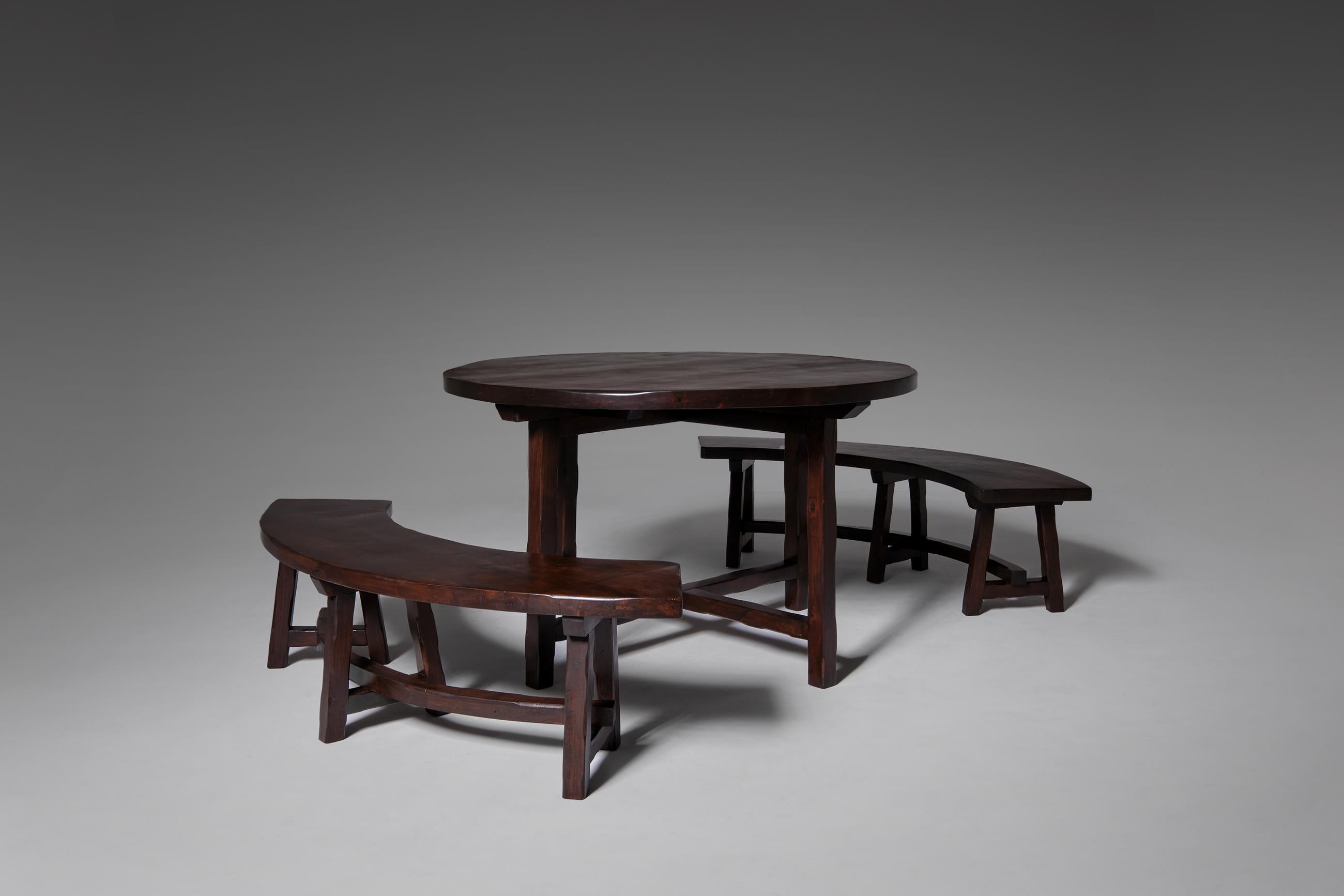 Primitive stained ash wooden table and two curved benches, France, 1970's. The set is constructed out of solid dark stained ash wood with nice warm tones. Every single element is carved by hand, this causes a very nice artisan character. Every bench