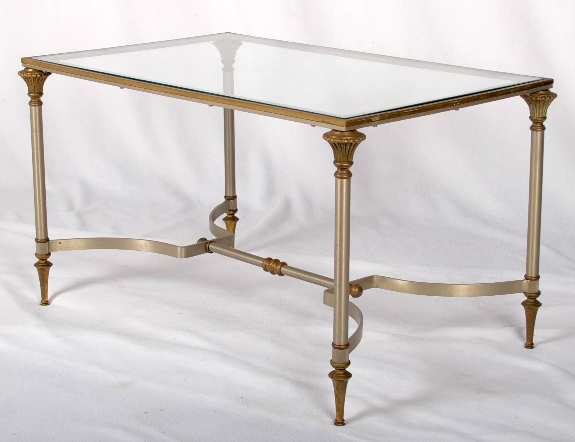 This is a lovely smallish coffee table with a glass top. It is in the style of Jansen of Paris.
The cast brass details are finely chiseled and well patinated. The brushed stainless frame is in excellent condition
 The glass top has a few small