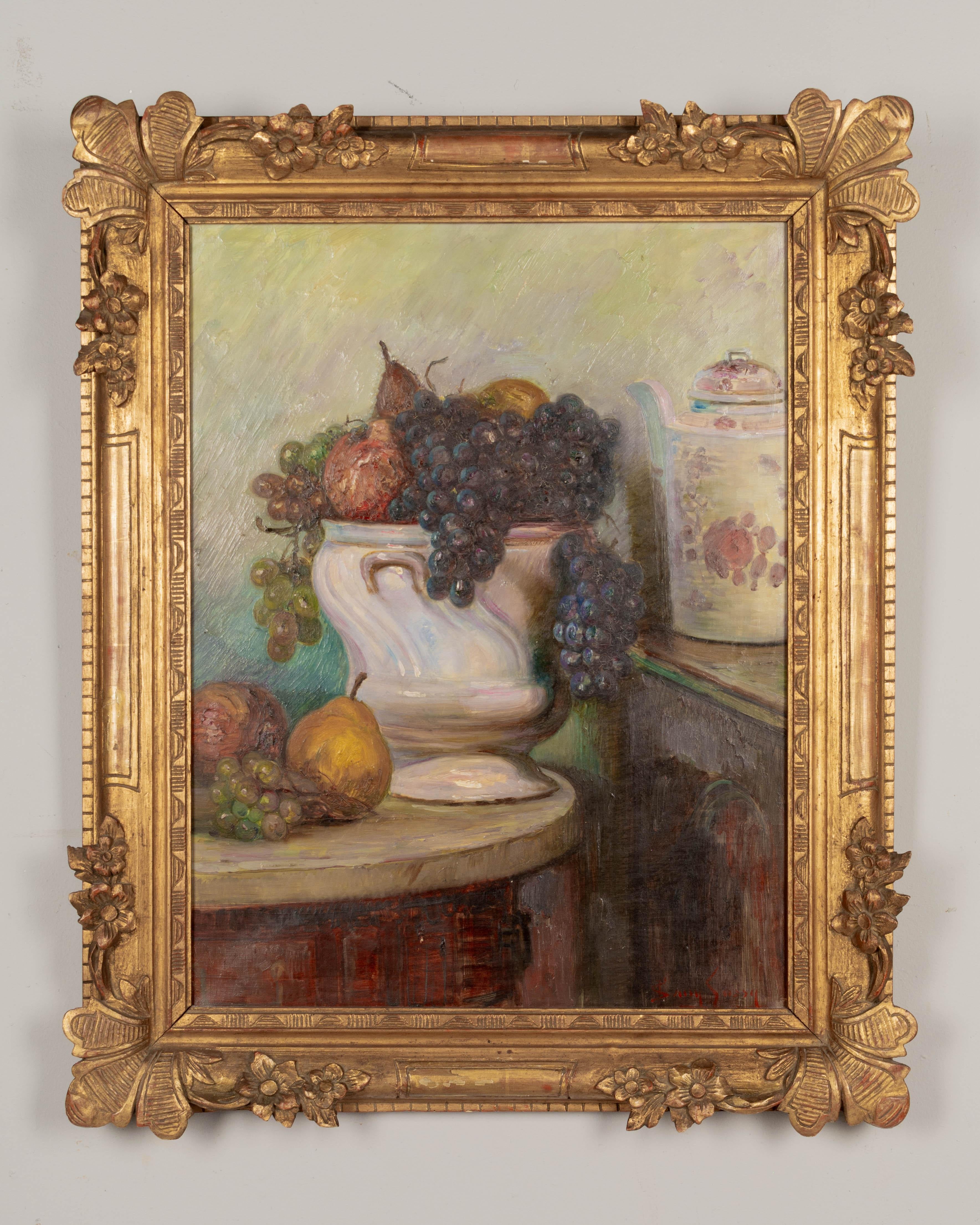 Nature morte de style impressionniste français représentant une grande coupe de fruits en porcelaine avec des raisins violets et verts, des poires et des pommes. Huile sur toile. Signé en bas à droite : Sany Sassy.  Cadre original en bois sculpté et