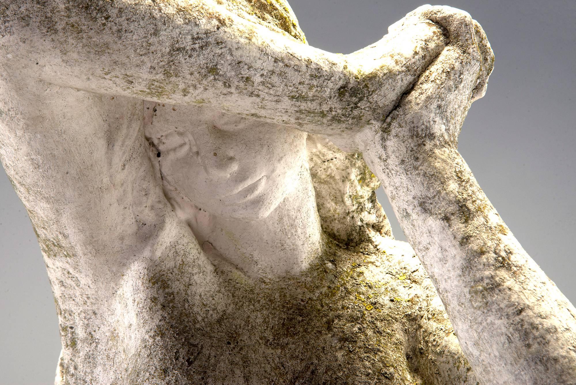 French stone garden statue depicts a long-haired nymph in a gown with her hands clasped and arm shielding her face. White wash finish has age-related patina and moss. Statue has a coordinating plinth base and with the base the piece stands just over