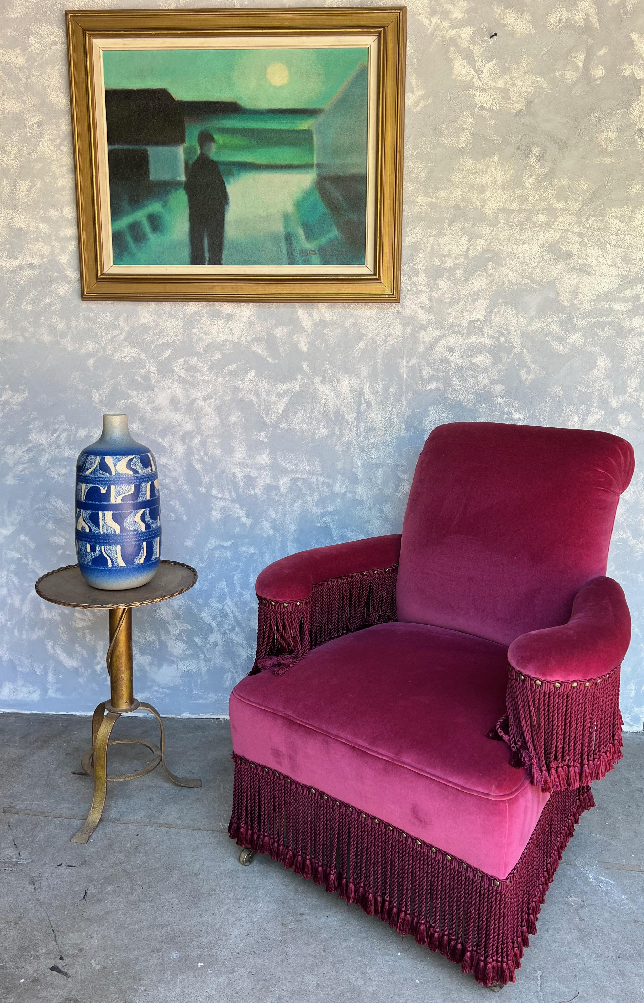 A very unusual armchair in the French style that is upholstered in a rich burgundy and trimmed with matching bouillon fringe the arms as well as at the bottom. The chair is in very good vintage condition and can be used as is. Most likely made in