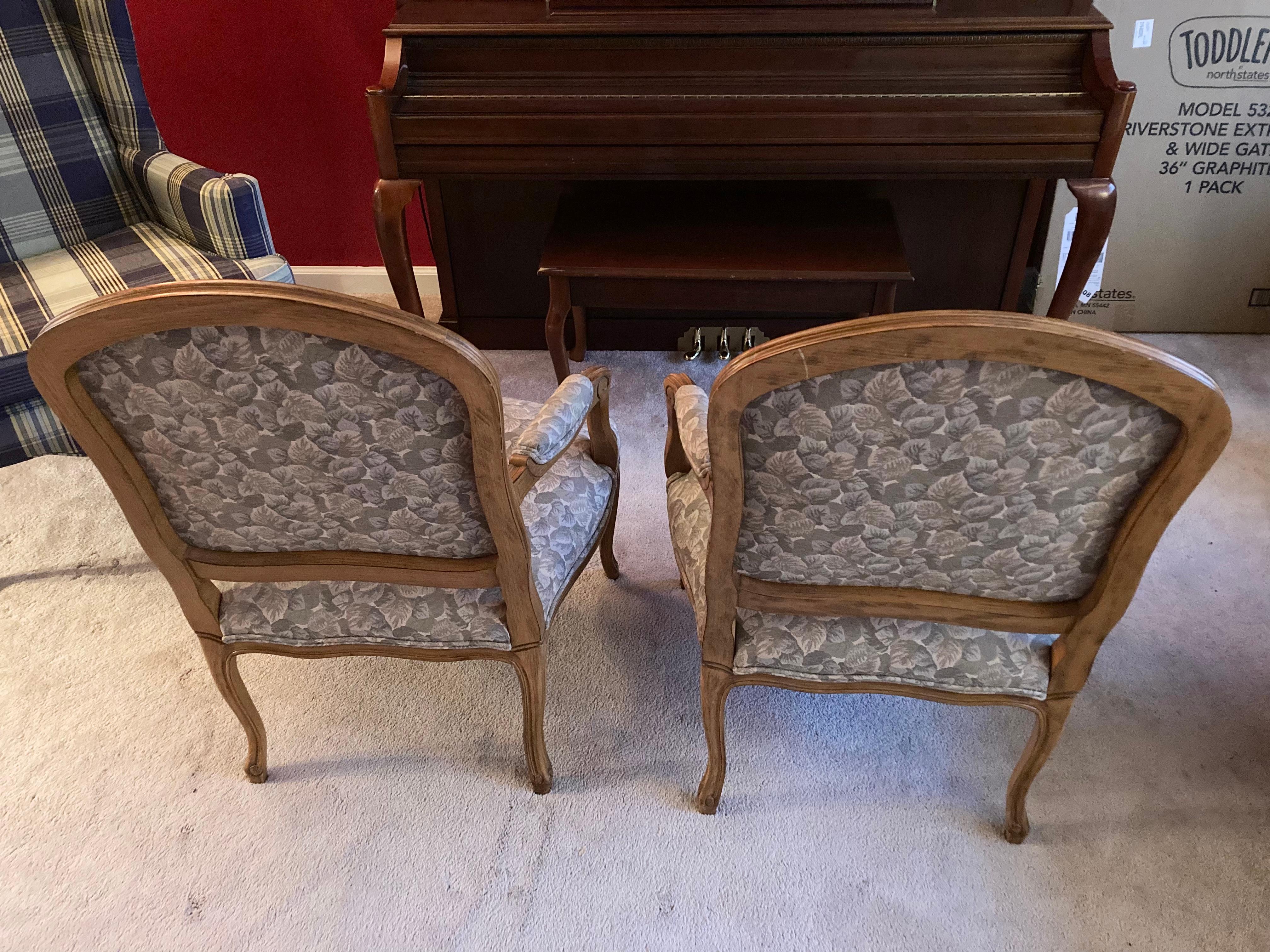 French style bergere chairs, a pair. Two blonde wood bergere armchairs, upholstered with piping. Simple carved details at arms and feet with padded elbow rests each side.