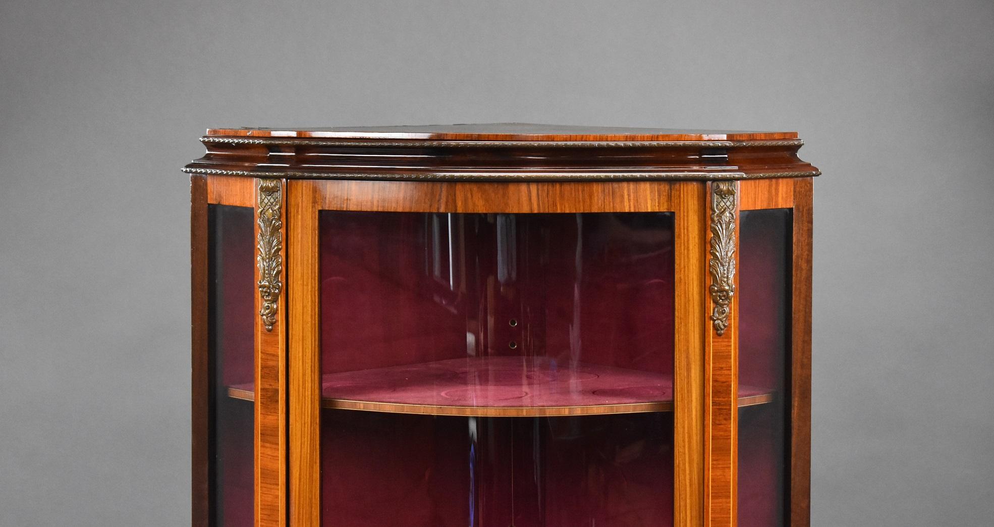 French style bow fronted corner cabinet in good condition with ormolu style mounts to the top and bottom with a flower decoration. The cabinet has three shelves covered in a dark pink fabric.