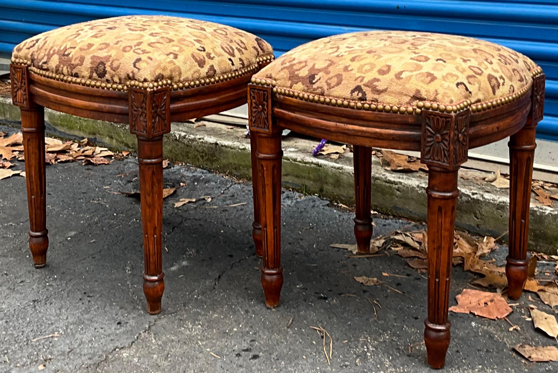 This is a pair of French style carved fruitwood ottomans in leopard needlepoint. They date to the later part of the 20th century and are unmarked.