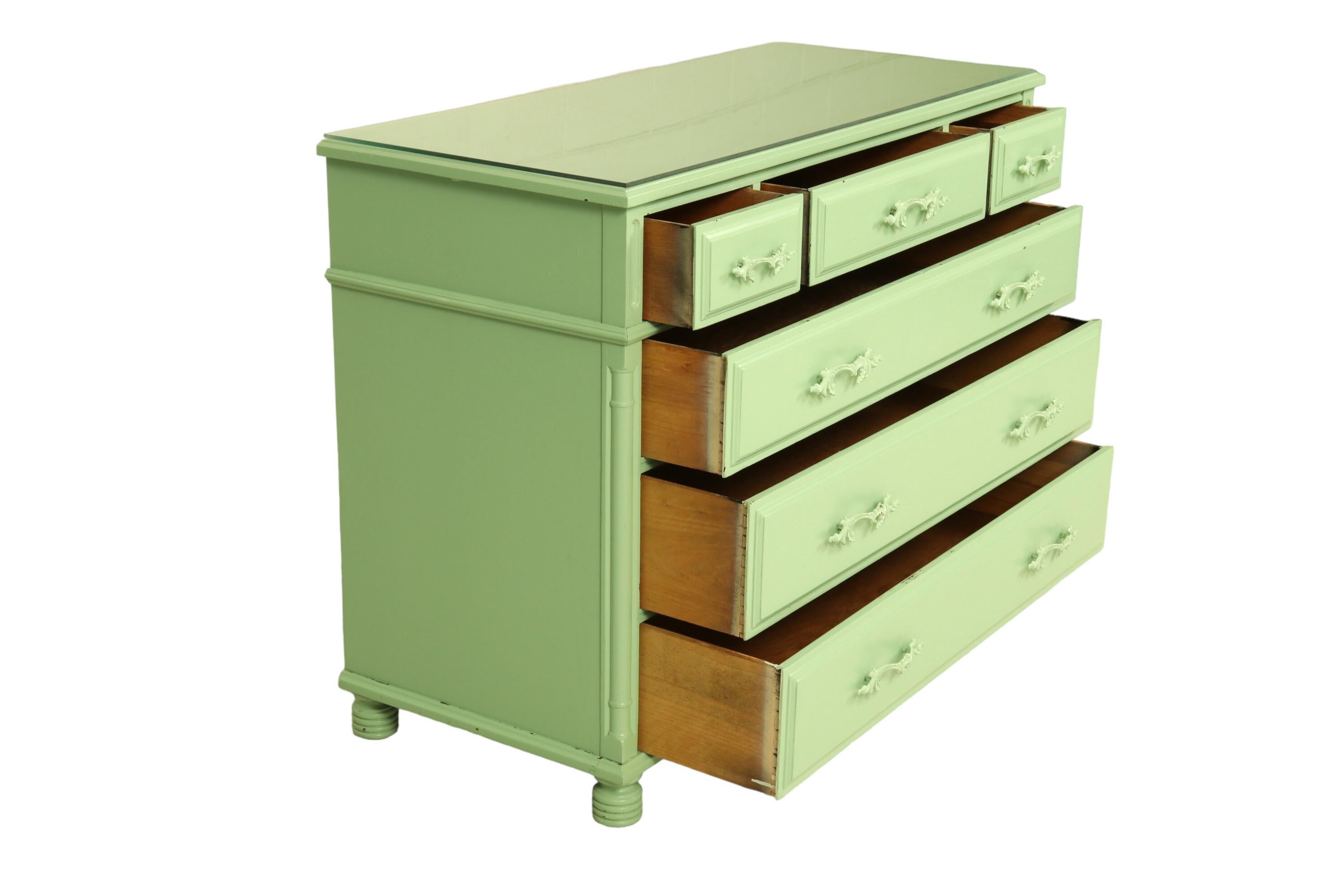 A French style chest of drawers in sage green. Three over three dovetailed drawers open with rococo metal handles, pressed with a c-scroll, shell like details and acanthus leaves. Corners are carved with inset cartouche panels above carved columns.