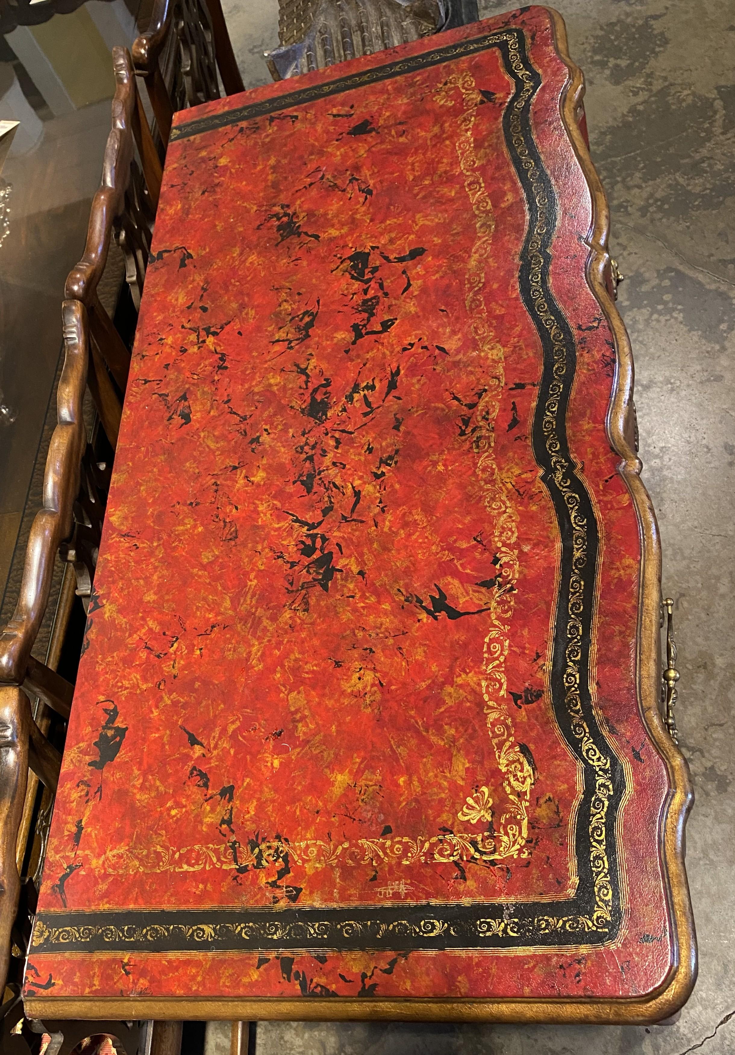 Una bellissima cassettiera a tre cassetti in stile francese con fronte a serpentina e superficie in finta pelle rossa lavorata, con accenti neri e dorati a contrasto, fianchi a pannelli sagomati, pesanti tiretti e rosette decorative in ottone e una