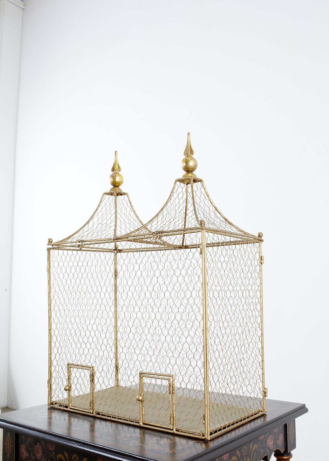 Distinctive metal and chicken wire bird cage featuring a gilt or gilded metal finish. Made in the French style with twin peaked roof that opens and topped with two large finials. Ball finials decorate each corner of the roof and the cage is fronted