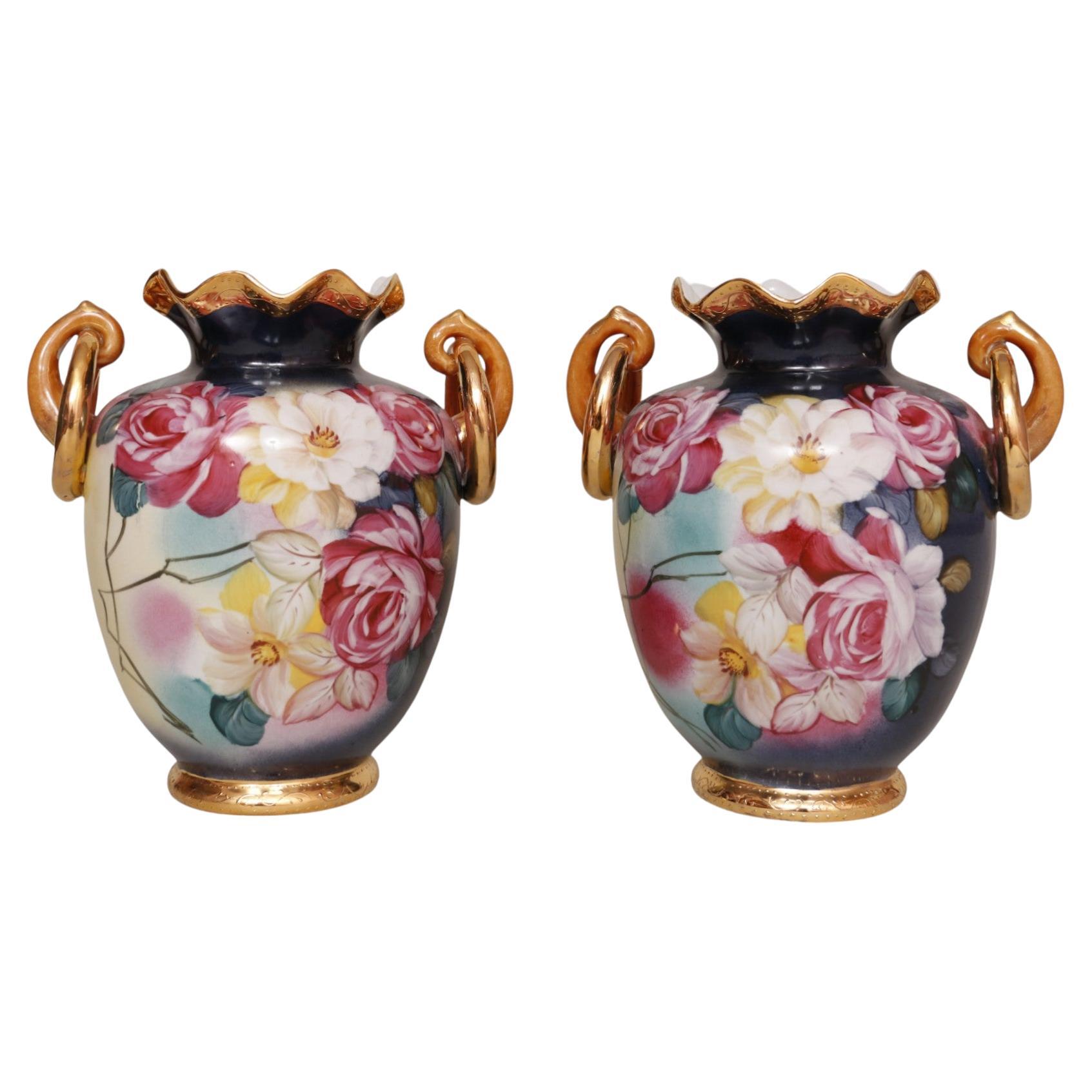 Coppia di vasi floreali in ceramica a forma di anfora in stile francese. Dipinto a mano con rose rosa, bianche e gialle su uno sfondo color crema e blu ammiraglio. Il vaso ha un labbro arruffato dorato e un piede dorato, entrambi decorati con punti