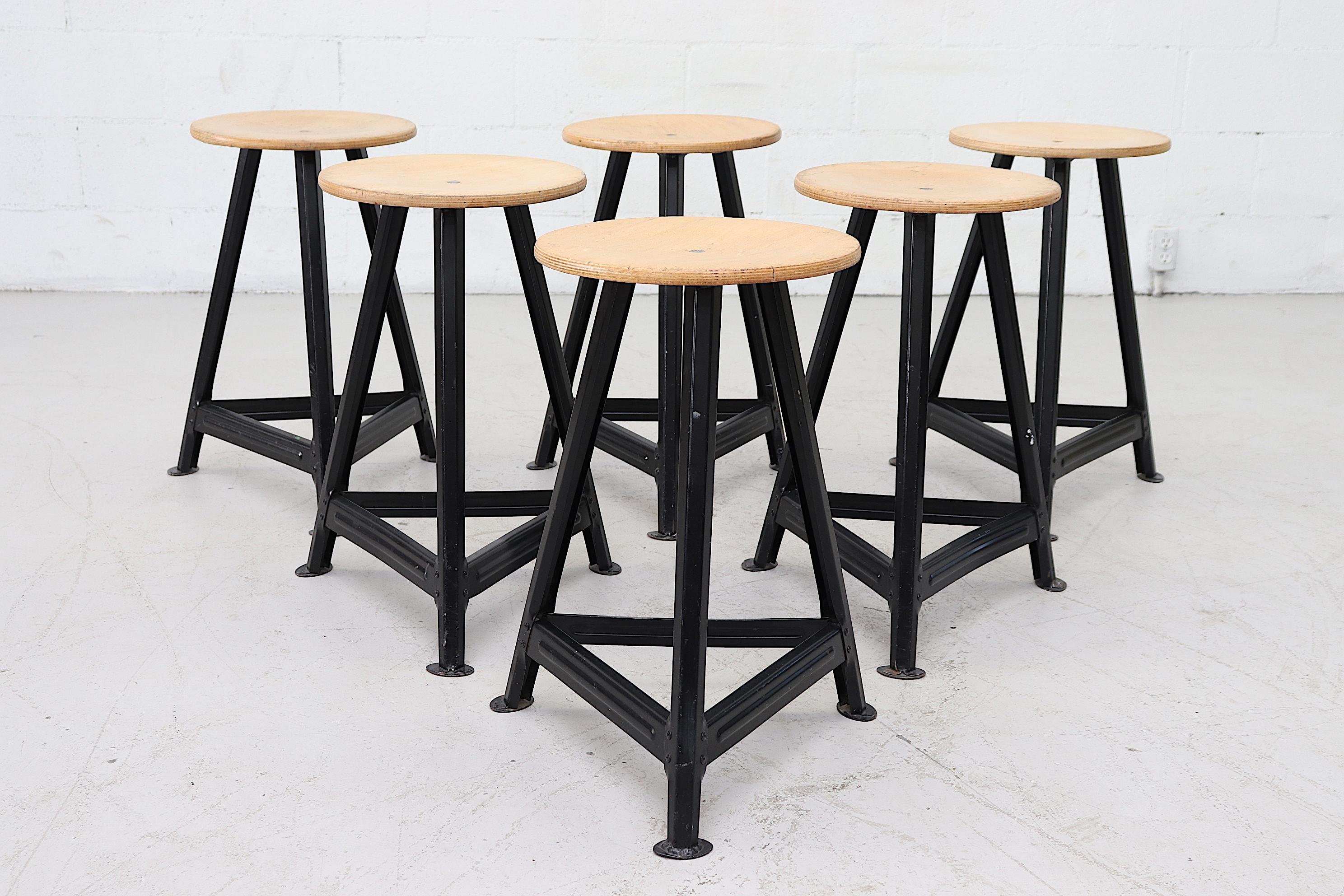 Industrial task stools with round plywood seats and black enameled metal bases. In original condition with some signs of wear consistent with age and use. Individually priced.