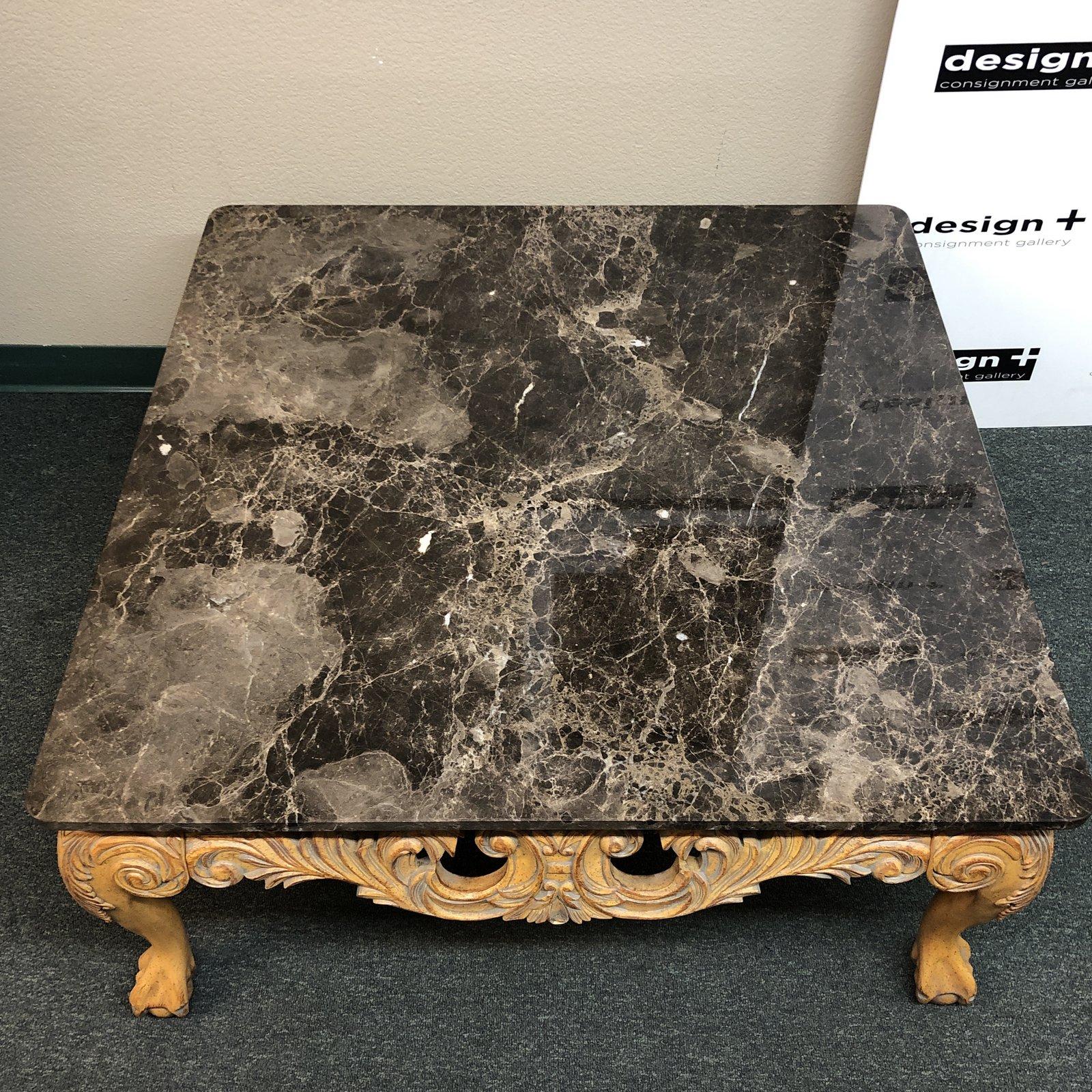 A large old world cocktail table. Crowned with a thick slab of richly veined brownish-gray and white marble, the intricately carved wood base has a gilt wash.