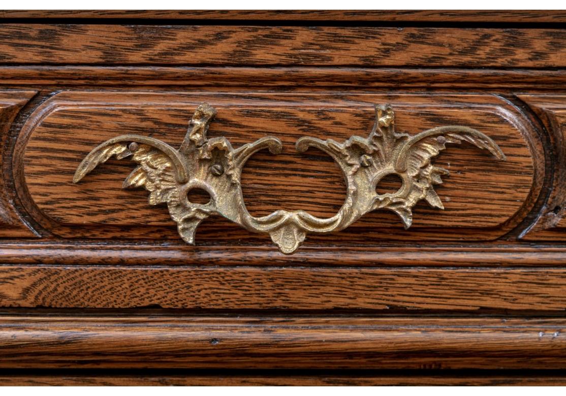 A very well made Oak chest in French Provincial style. With overhanging top and two short over three long drawers, all carved and with fine brass foliate bales and escutcheons (lacking a key). The shaped skirt rail with carved shell, and raised on