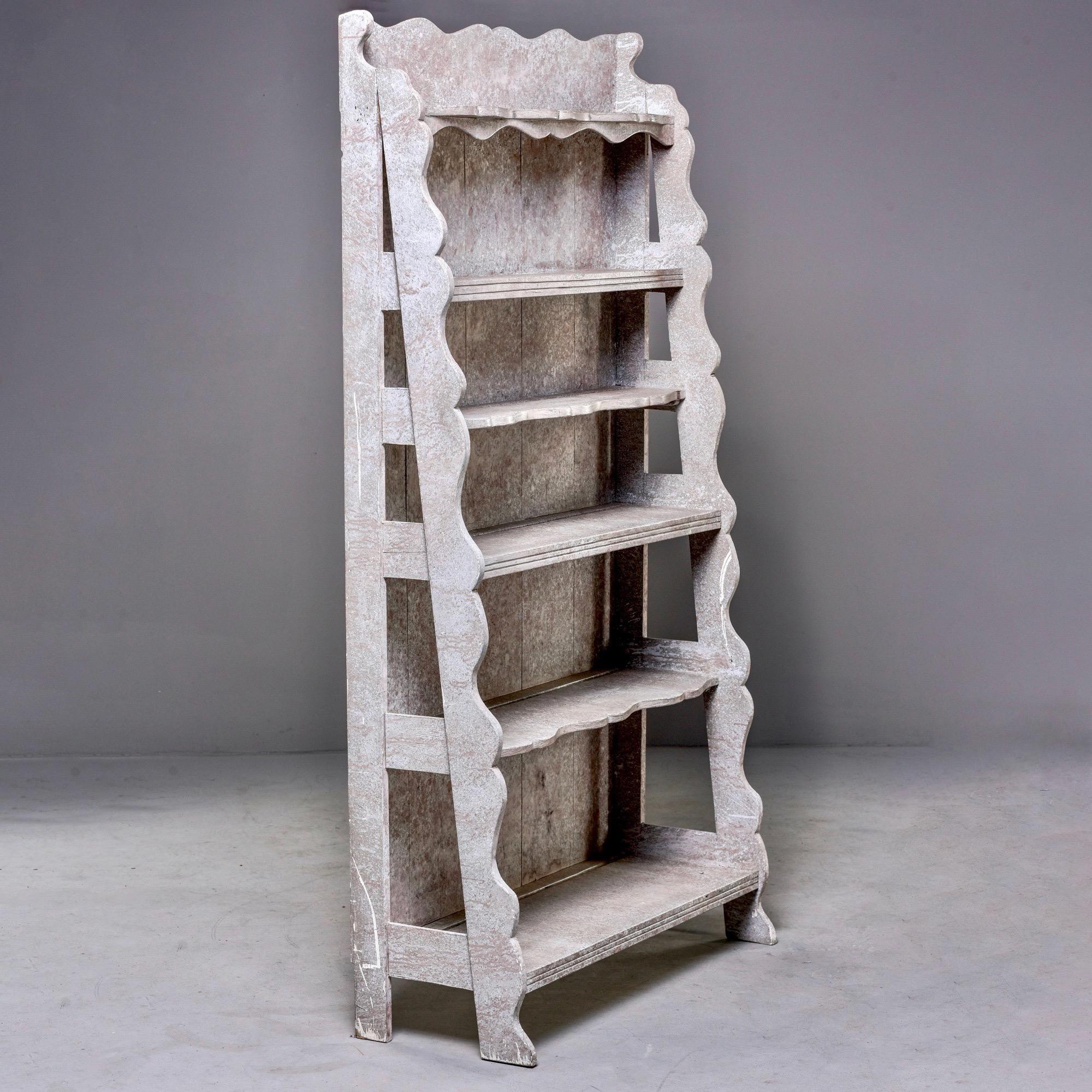 Freestanding painted wood shelf unit with loads of French style found in England, circa 2010. Very sturdy unit has five shelves in graduated height and depth with a footed base, decorative scalloped edges on side supports and top. Gray painted