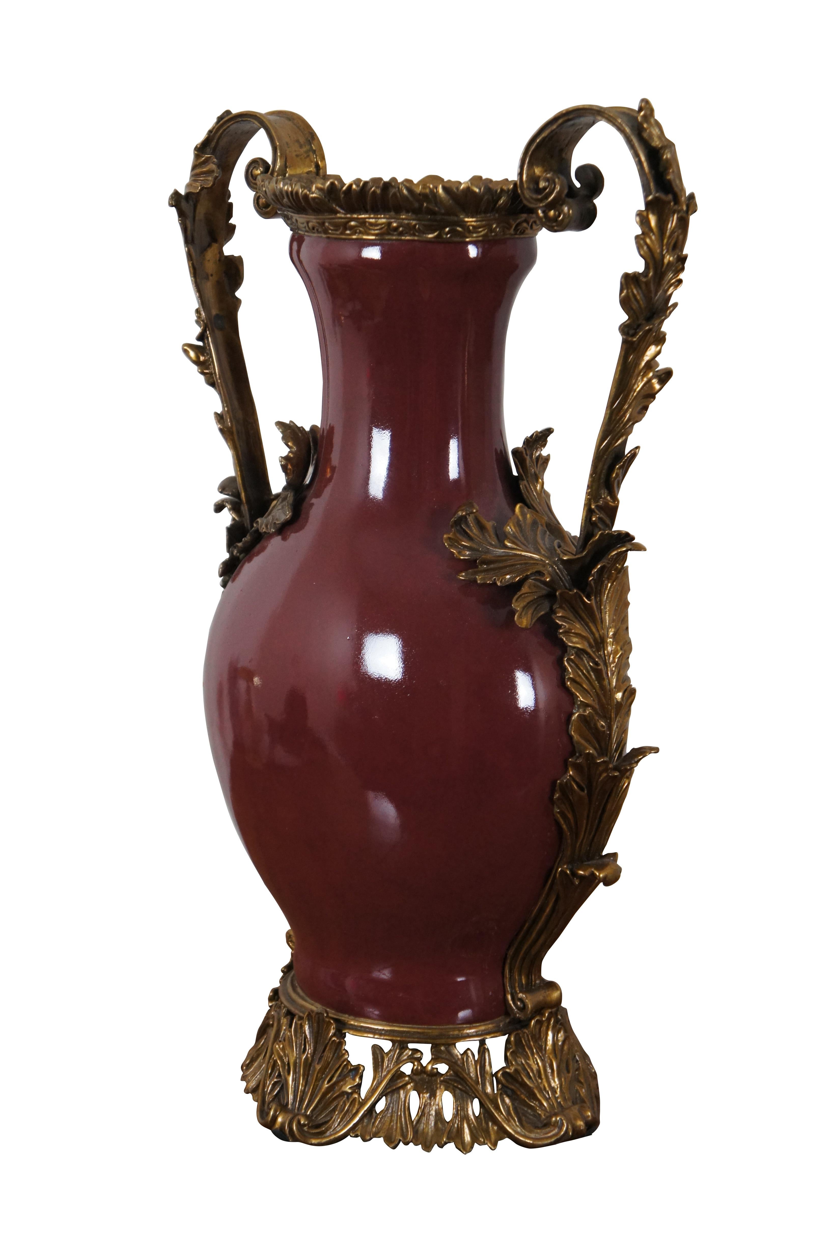 Late 20th century oxblood red porcelain vase with gilt bronze base, rim, and double handles in the manner of French inspired vase.  Features swirling foliate ormolu with acanthus leaves and scalloped accents. Made in China. Not for Food Use, for