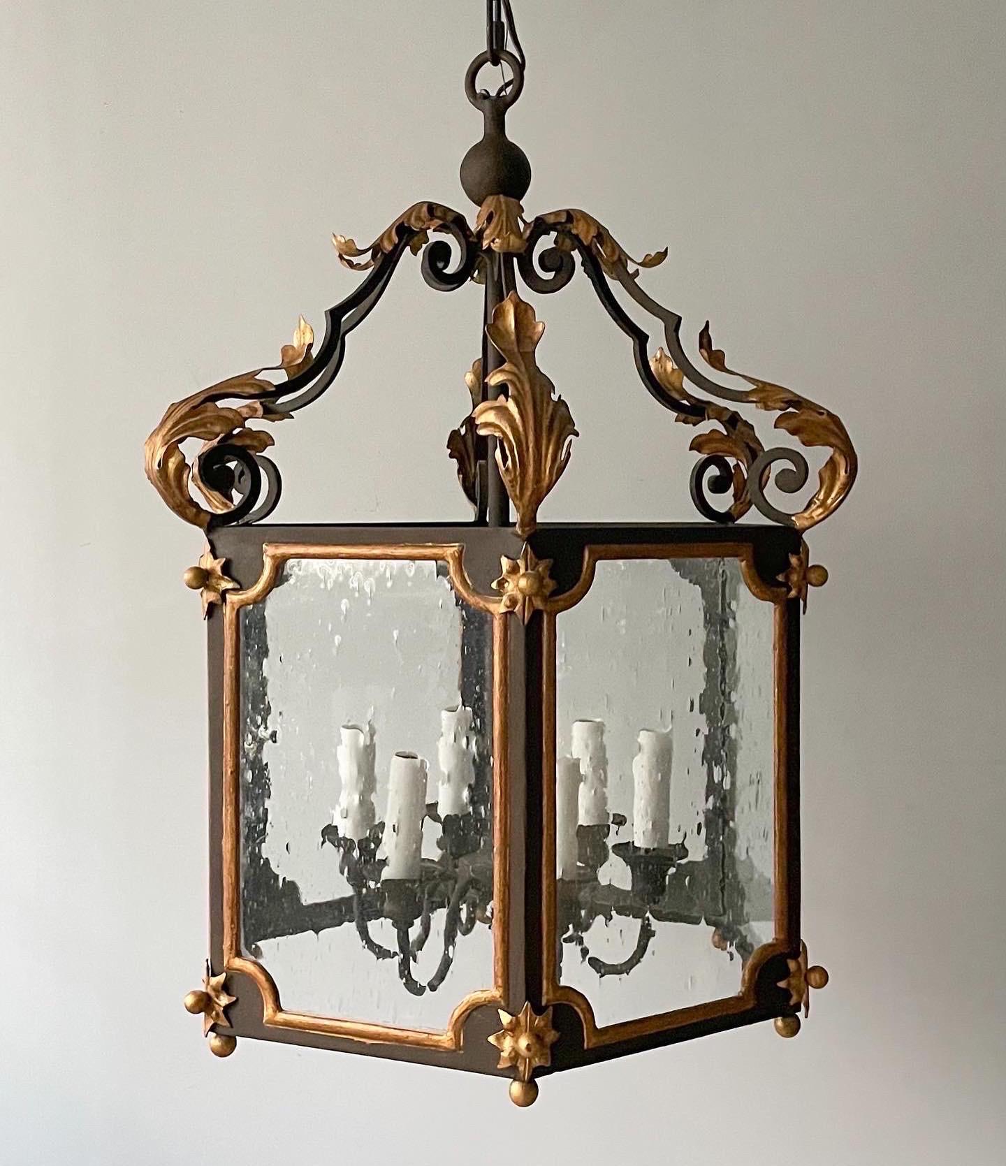 Gorgeous, vintage painted and parcel- gilt lantern in the French provincial style. 

The lantern feature an iron frame in a dark rusty brown finish with gilded decorations including acanthus leaves and stars. Seed glass panels. 

The lantern is