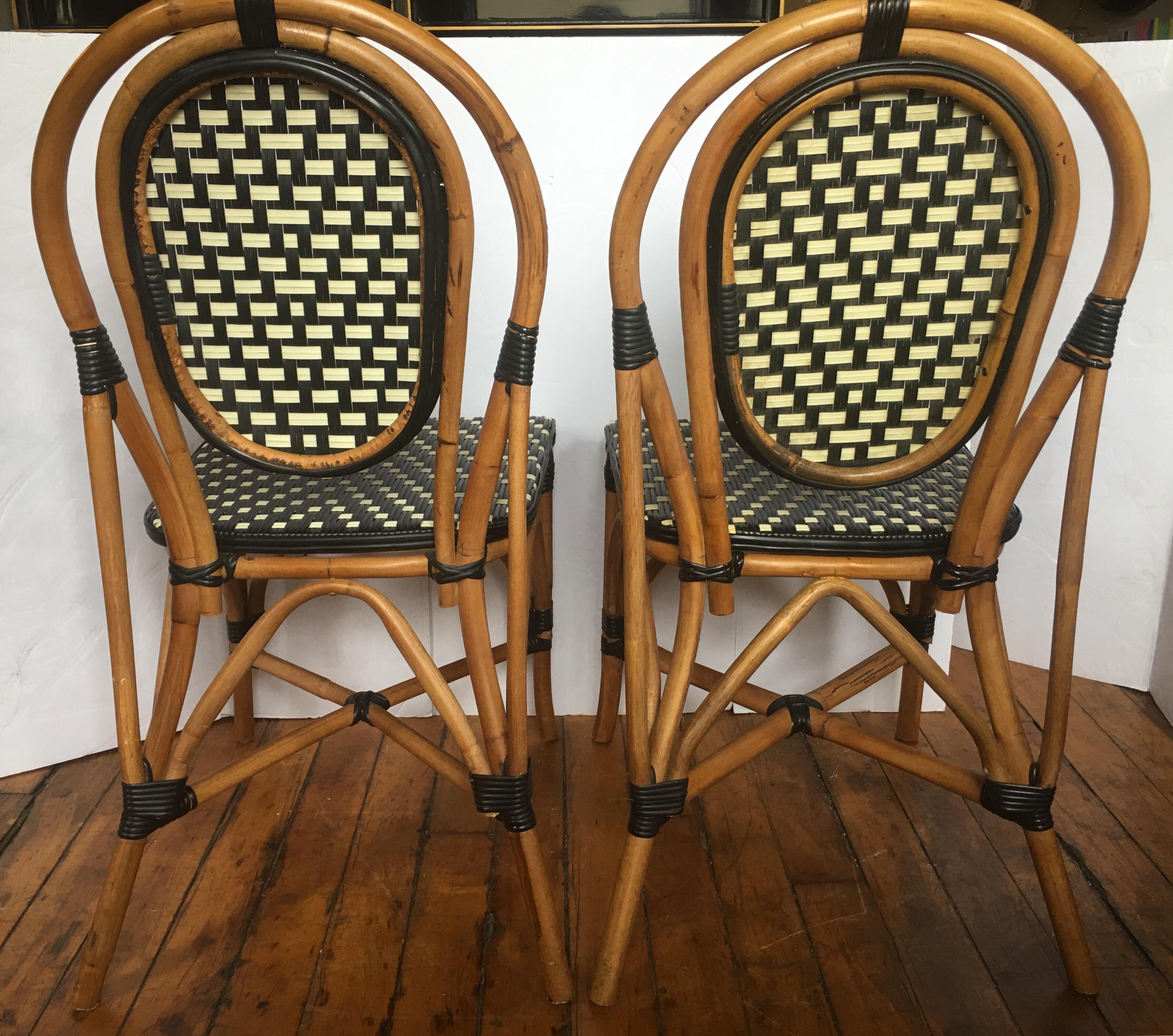 Pair of Classic French style bistro dining side chairs just like those you find in a Paris café. Frames expertly handcrafted of natural Malacca/Manau steamed bent cane with neutral black/ivory woven nylon seats and backs. For indoor and outdoor use
