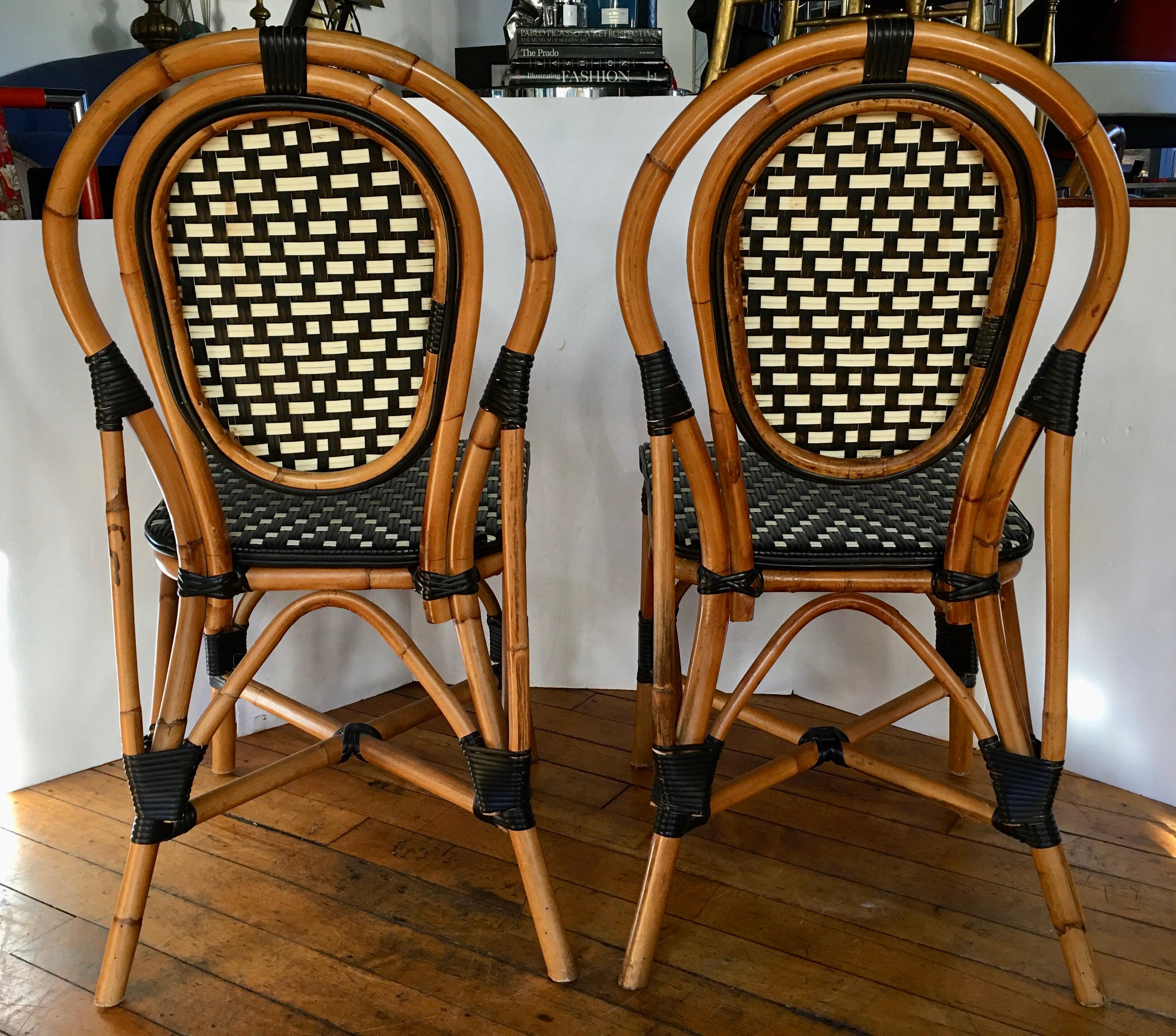 Pair of Classic French style bistro dining side chairs just like those you find in a Paris café. Frames expertly handcrafted of natural Malacca/Manau steamed bent cane with neutral black/ivory woven nylon seats and backs. For indoor and outdoor use