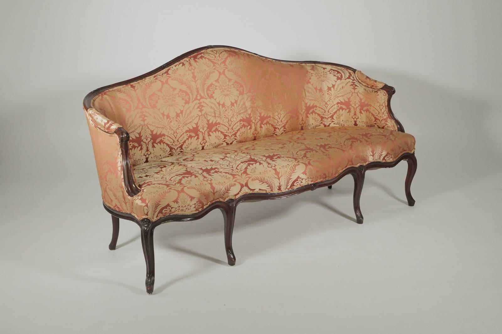 French style walnut serpentine sofa with recent damask upholstery. The graceful hand carved frame with gentle curves with eight hay hand tied springs. Wonderful medium size, and easy to care for attached seat and back.