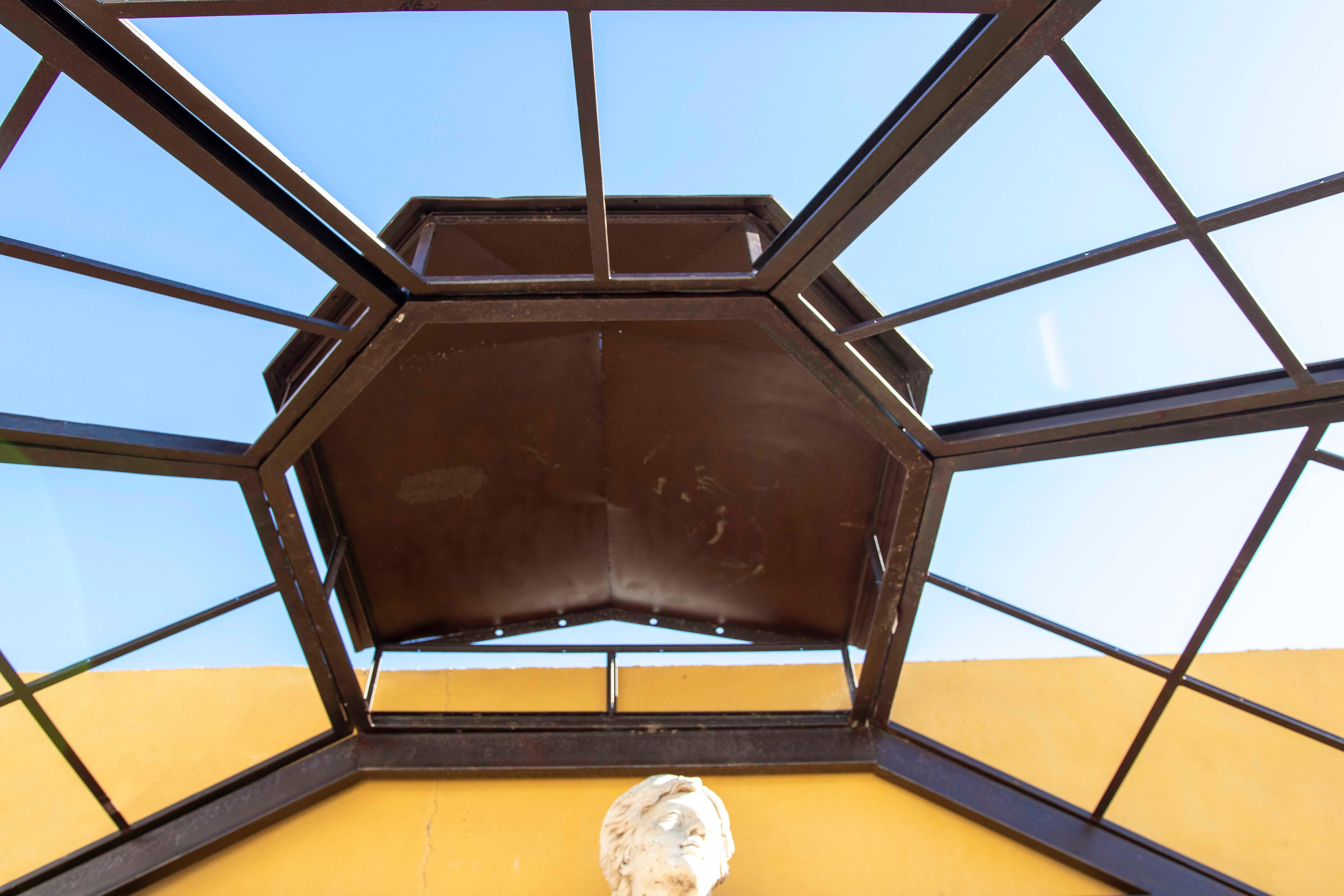 Elégante serre murale octogonale en fer forgé, parfaite pour créer un espace unique et sophistiqué dans les jardins, les patios ou les terrasses. Son design avec des arches et des panneaux décoratifs met en valeur un style classique intemporel. La