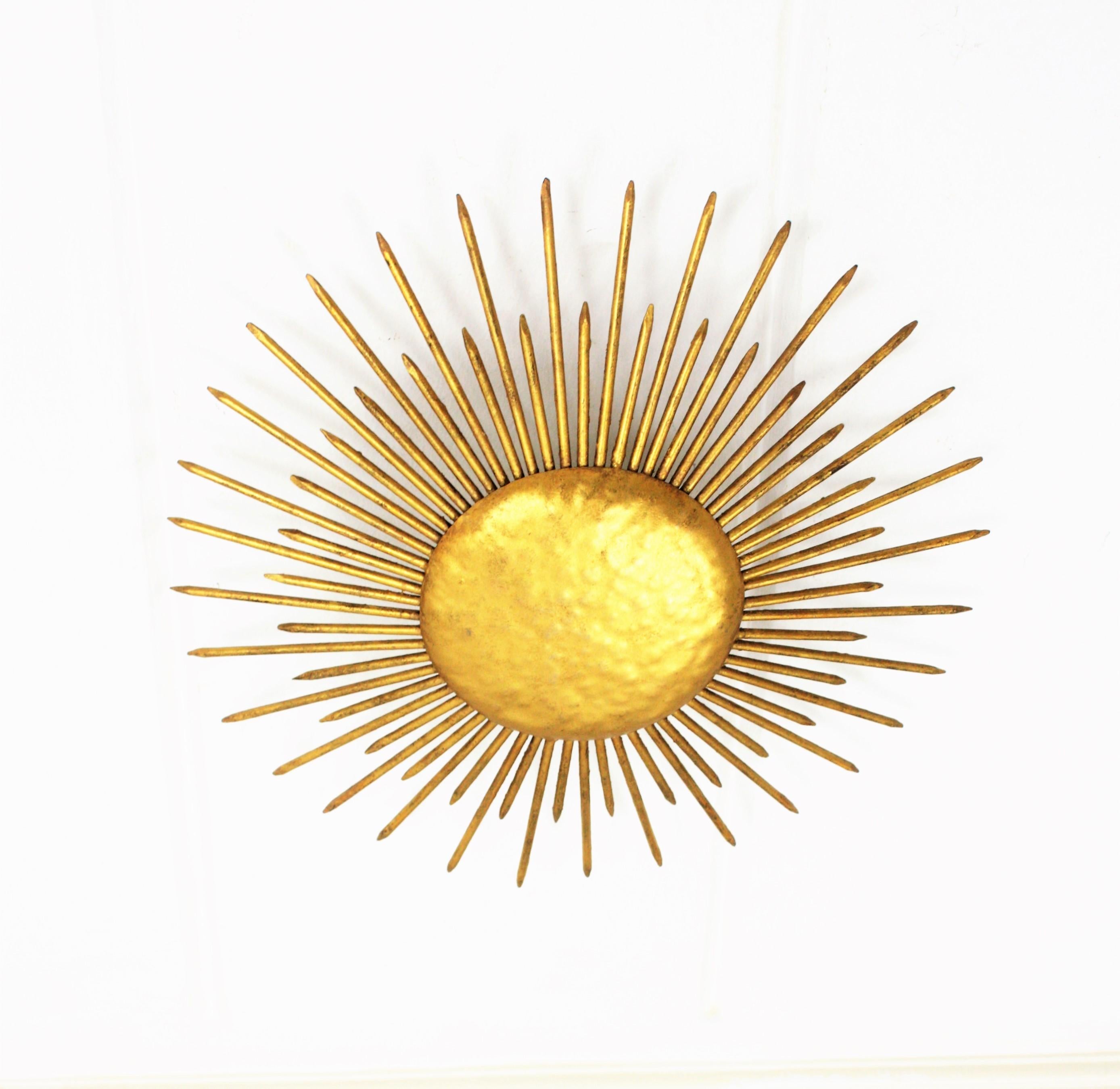 French wrought gilt iron sunburst light fixture with nails details. France, 1930s-1940s.
Gorgeous hand-hammered gilt iron sunburst ceiling light fixture or wall sconce with gold leaf finish and Art Deco accents in transition to Brutalist style. A