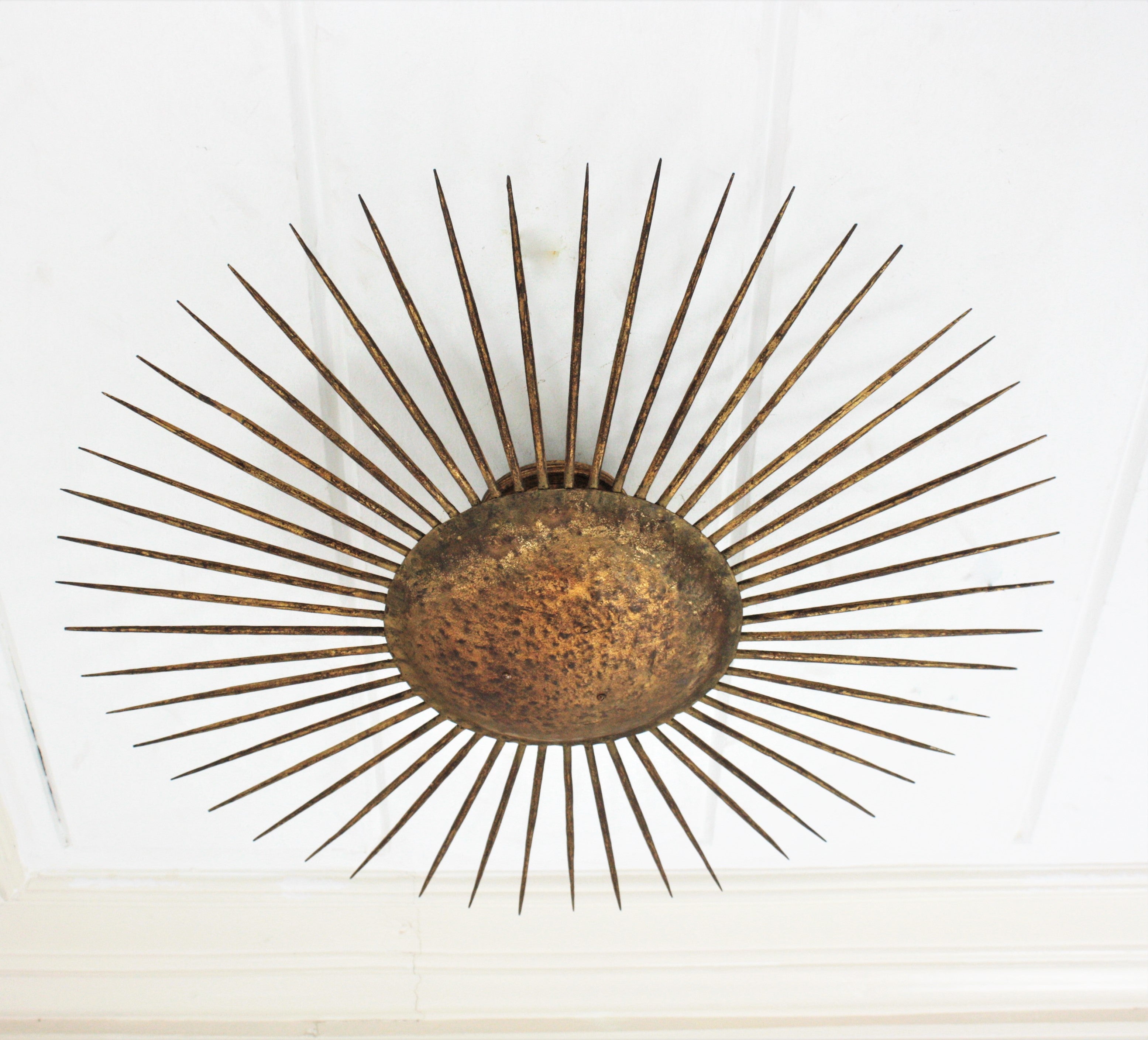 Large Sunburst flush mount, wrought iron, gold leaf, France, 1930s-1940s.
This iron sunburst ceiling flush mount was hancrafted at the late Art Deco period. It has a nice design with pointed spikes surrounding a central spherical plate. Entirely