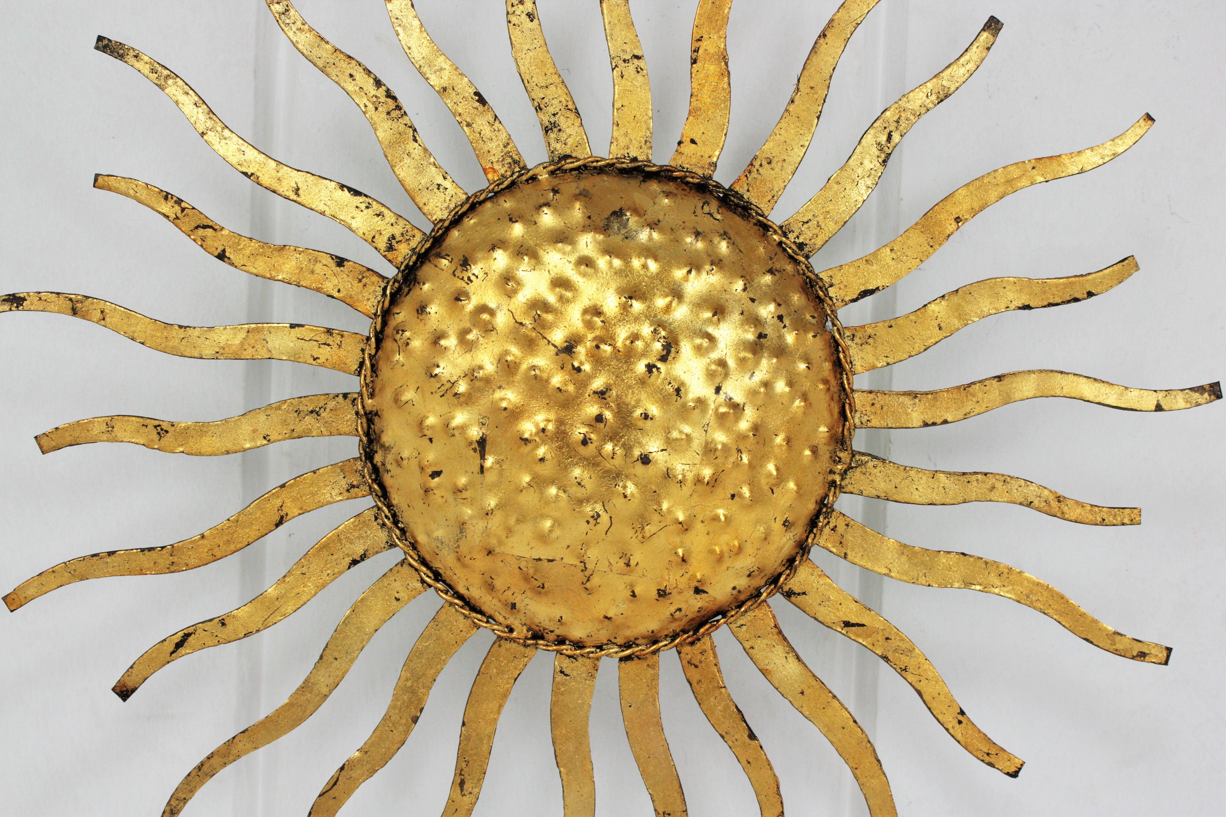 Wrought gilt metal sunburst ceiling lamp or light fixture, France, 1950s.
This hand-hammered iron flushmount is heavily adorned by the hammer marks at the central sphere and it has alternating rays in two sizes.
All handcrafted in iron with gold