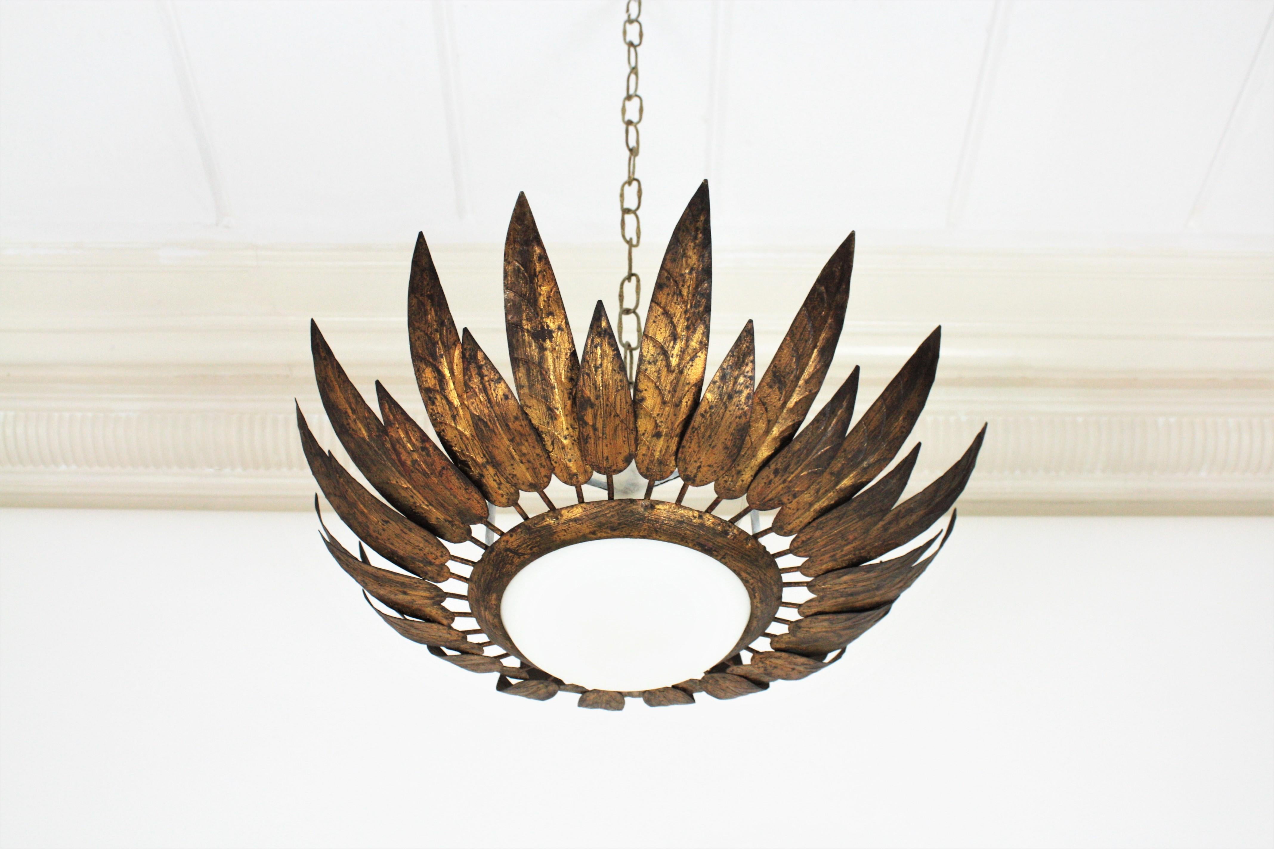 Gold leaf gilt iron flower shaped sunburst light fixture with leafed / feathers frame, France, 1950s
This lovely flush mount was manufactured at the Mid-Century Modern period in the style of Hollywood Regency. 
It has alternating short and long