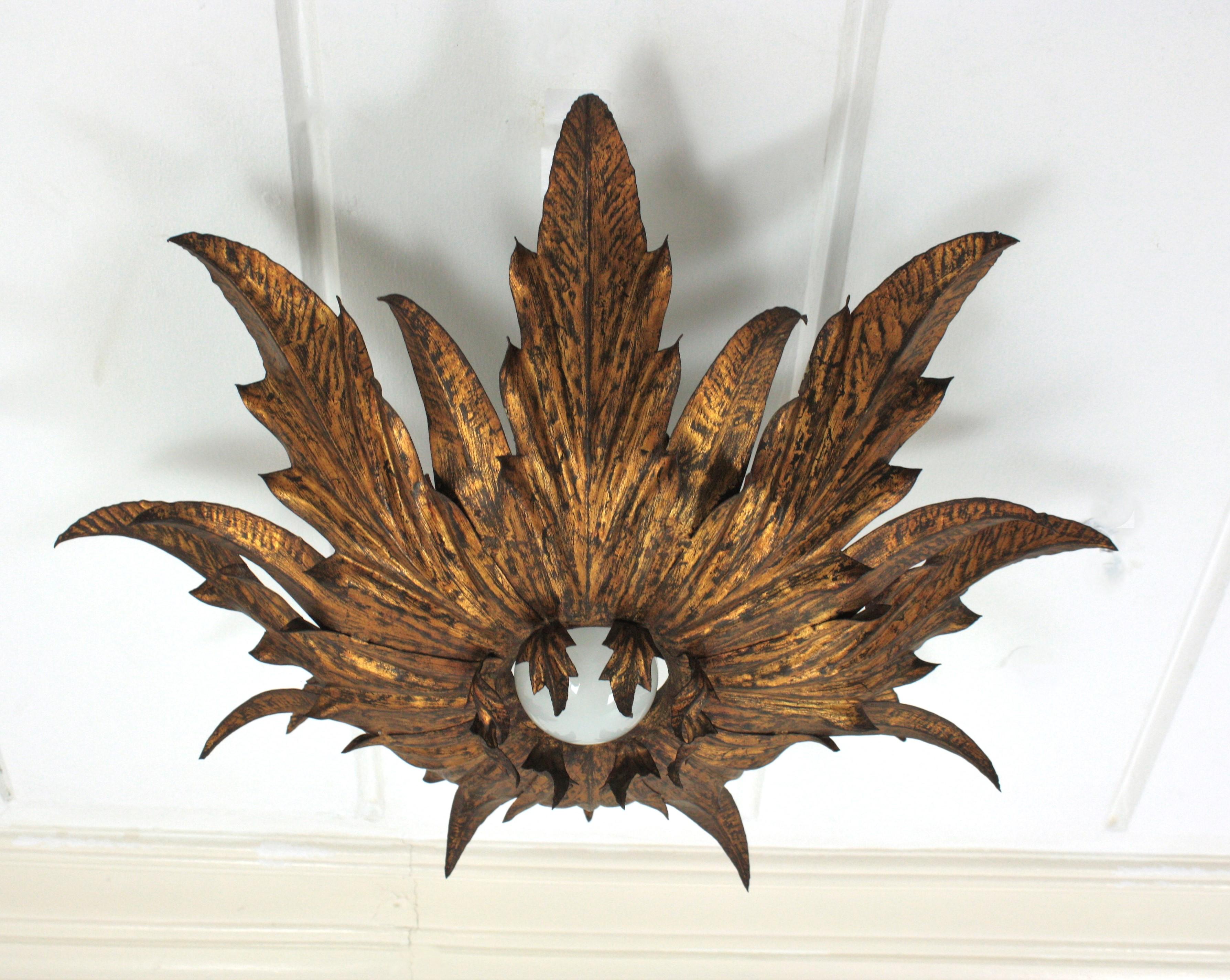 Stunning flower or sunburst ceiling light fixture, gilt iron, gold leaf, France, 1940s-1950s.
Large size.
This eye-catching ceiling lamp features a double layered leafed frame of leaves surrounding a central exposed bulb. A layer of small curved