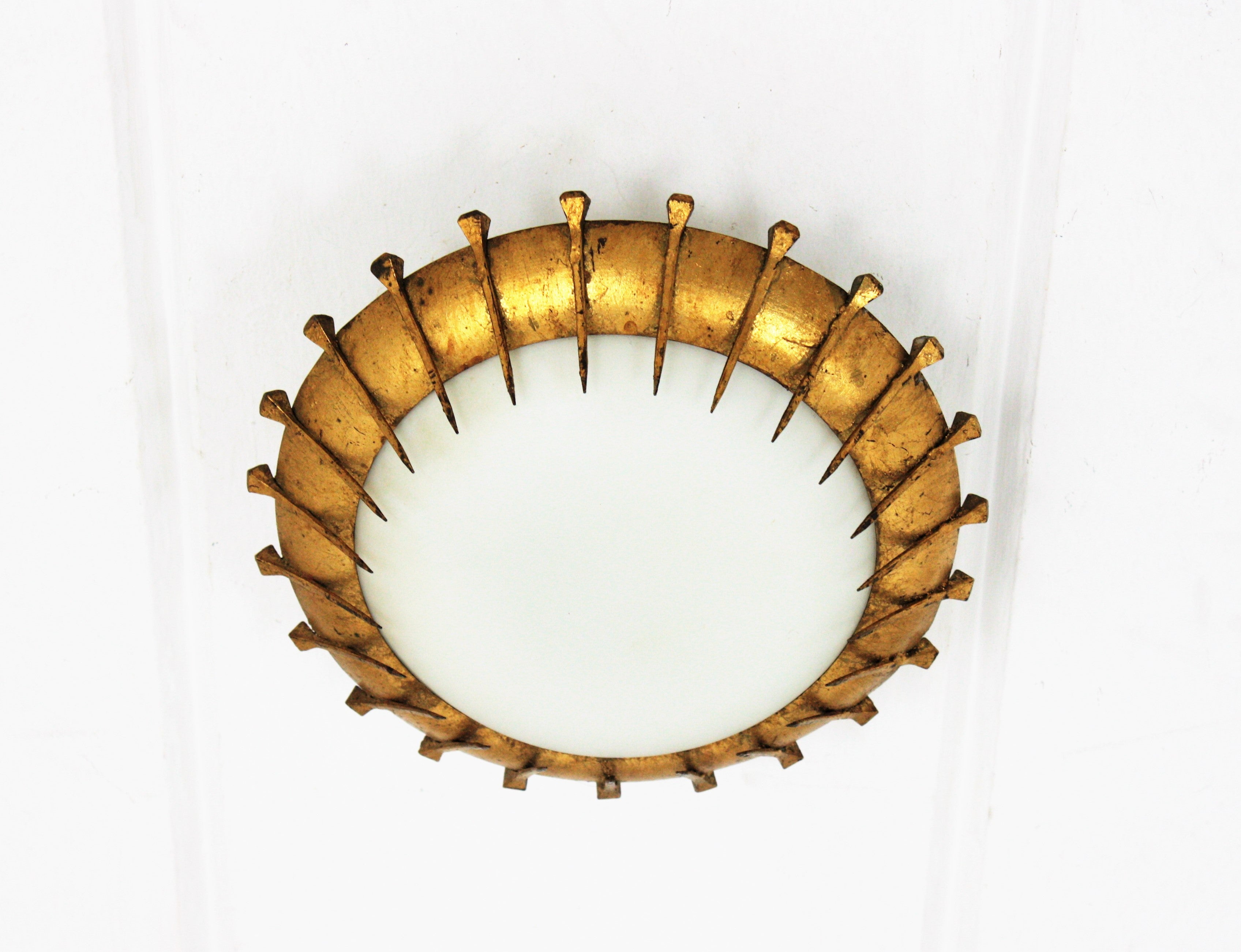 Nail Design sunburst flush mount, gilt wrought iron, milk glass, France, 1940s-1950s.
Hand-hammered iron and opaline glass sunburst flush mount with nails decoration and gold leaf finish. 
Beautiful to place it alone but also interesting mixed