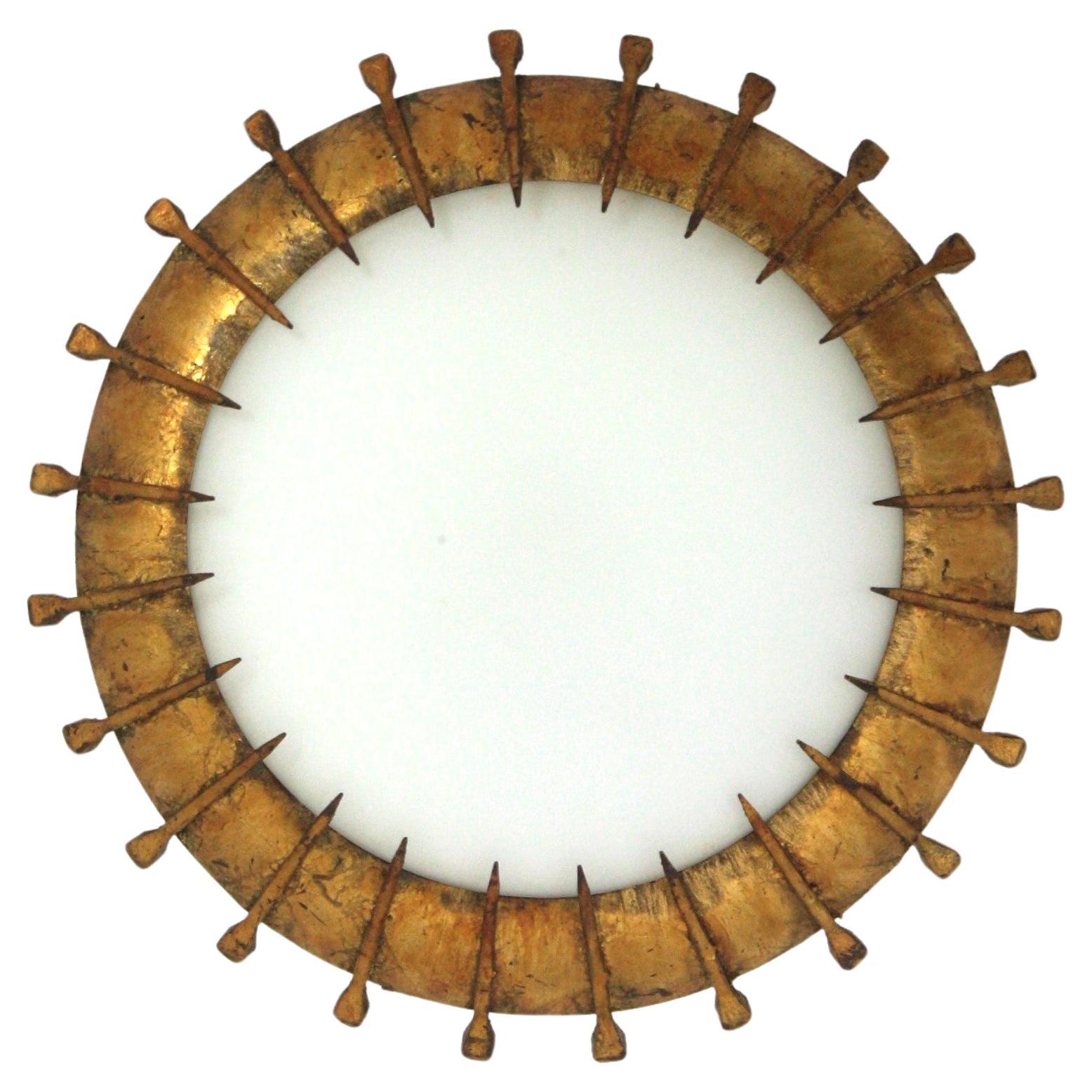Nail Design sunburst flush mount, gilt wrought iron, milk glass, France, 1940s-1950s.
Hand-hammered iron and opaline glass sunburst flush mount with nails decoration and gold leaf finish. 
Beautiful to place it alone but also interesting mixed with