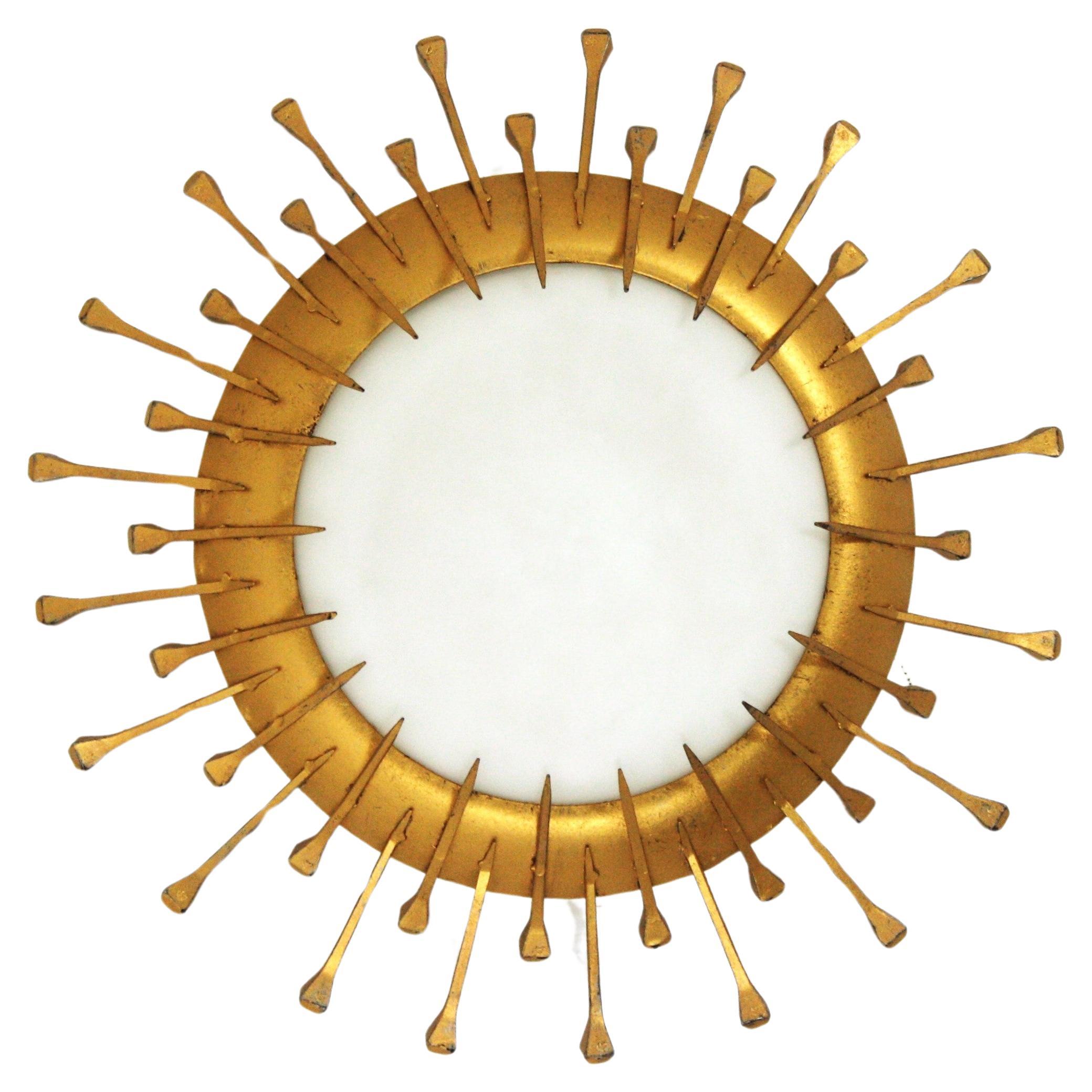 Eye-catching hand-hammered iron and opaline glass sunburst flush mount / wall light. France, 1940s-1950s.
This sunburst light fixture features two layers of alternating short and long nail decoration and gilt finish. Style in transition from Art