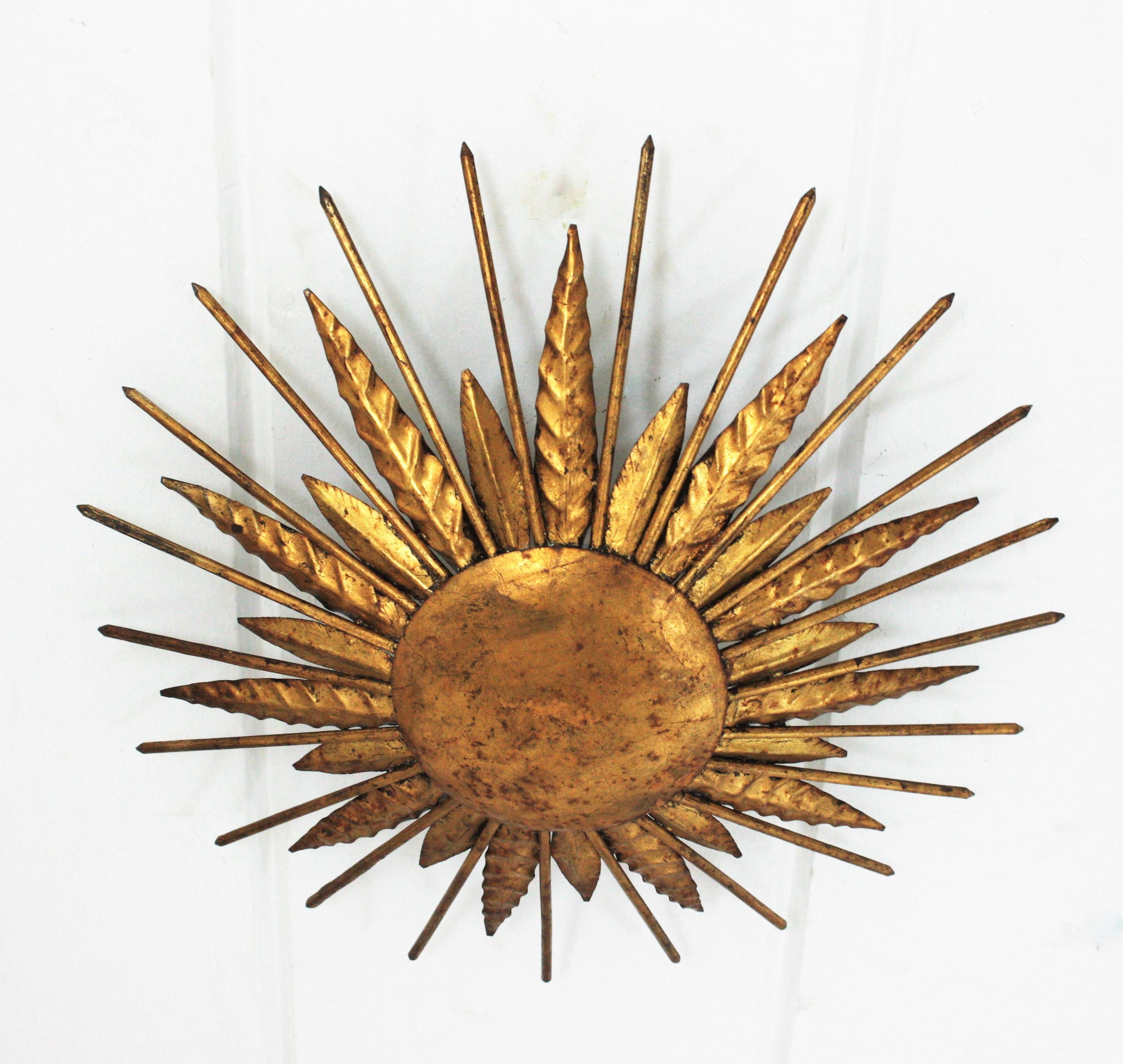 French modern neoclassical sunburst flush mount / wall light in gilt iron with spikey gilt nail rays. France, 1940s.
Outstanding hand-hammered gold leaf gilt iron leafed sunburst light fixture from the late Art Deco period.
Highly decorative