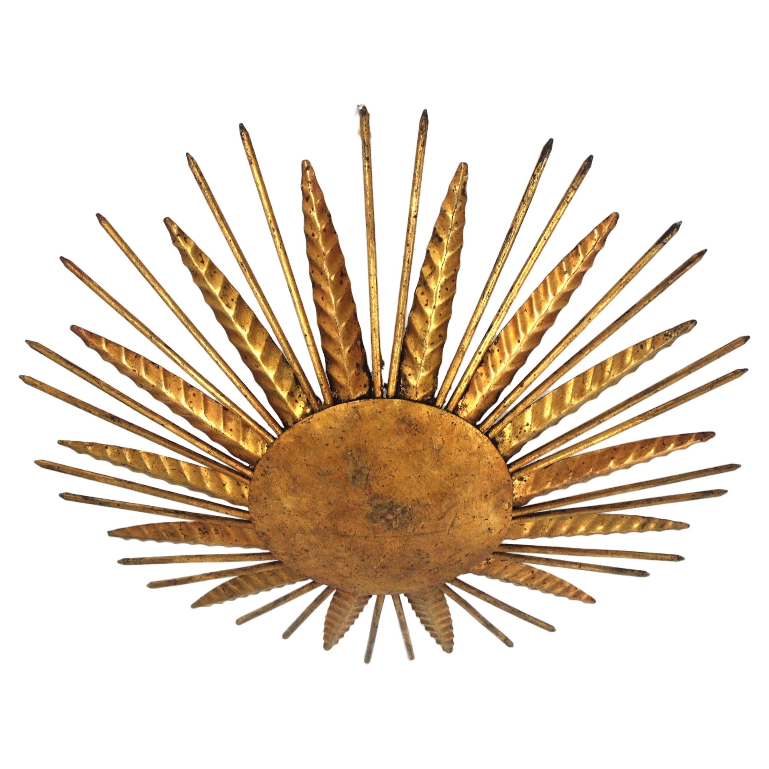 French modern neoclassical sunburst flush mount / wall light in gilt iron with spikey gilt nail rays. France, 1940s.
Outstanding hand-hammered gold leaf gilt iron leafed sunburst light fixture from the late Art Deco period.
Highly decorative design