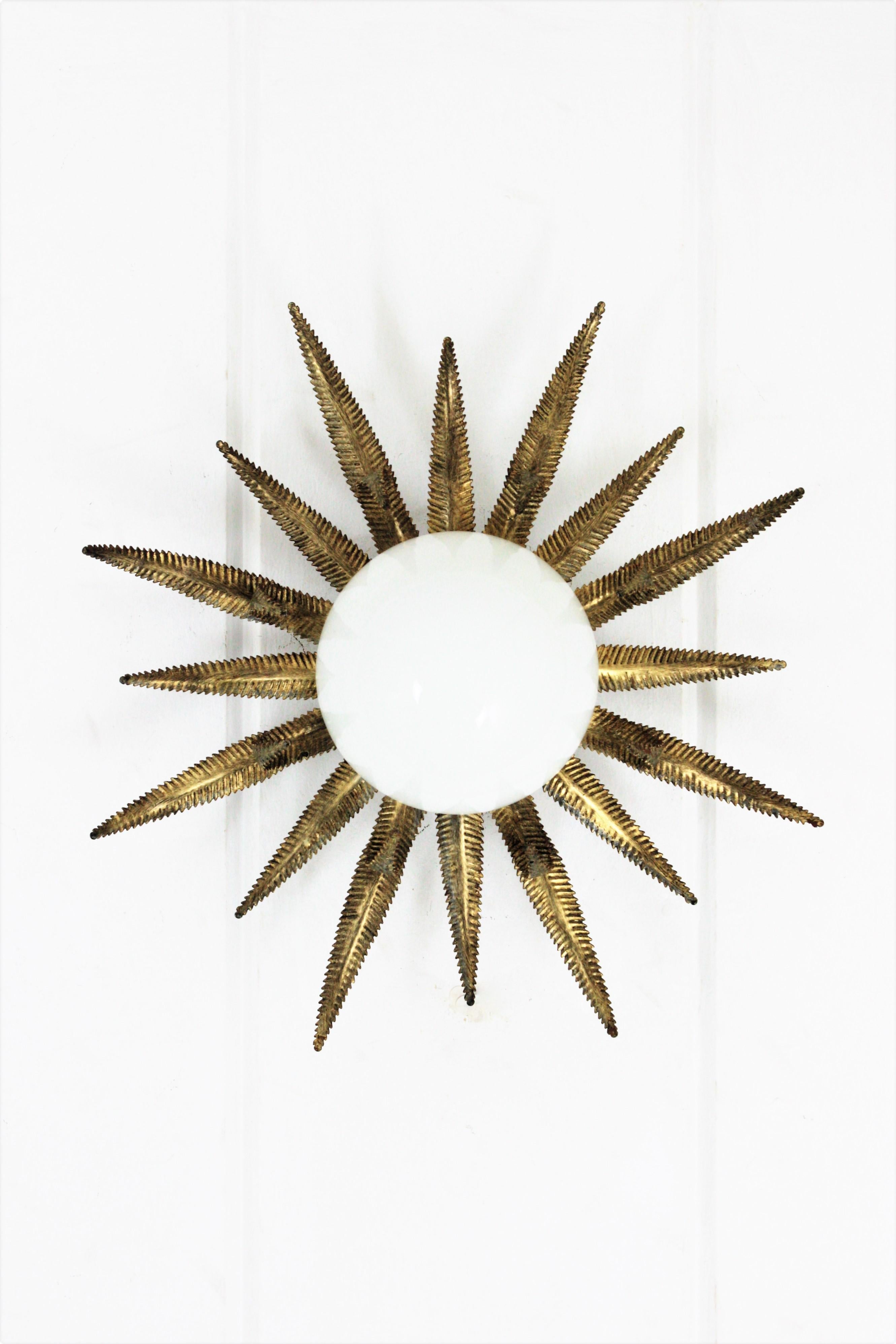 Outstanding French sunburst flush mount in gilt metal and milk glass, 1950s
This Sunburst starburst ceiling light fixture has an eye-catching construction. The sunburst backplace in patinated gilt and sunburst or starburst shape holds a
