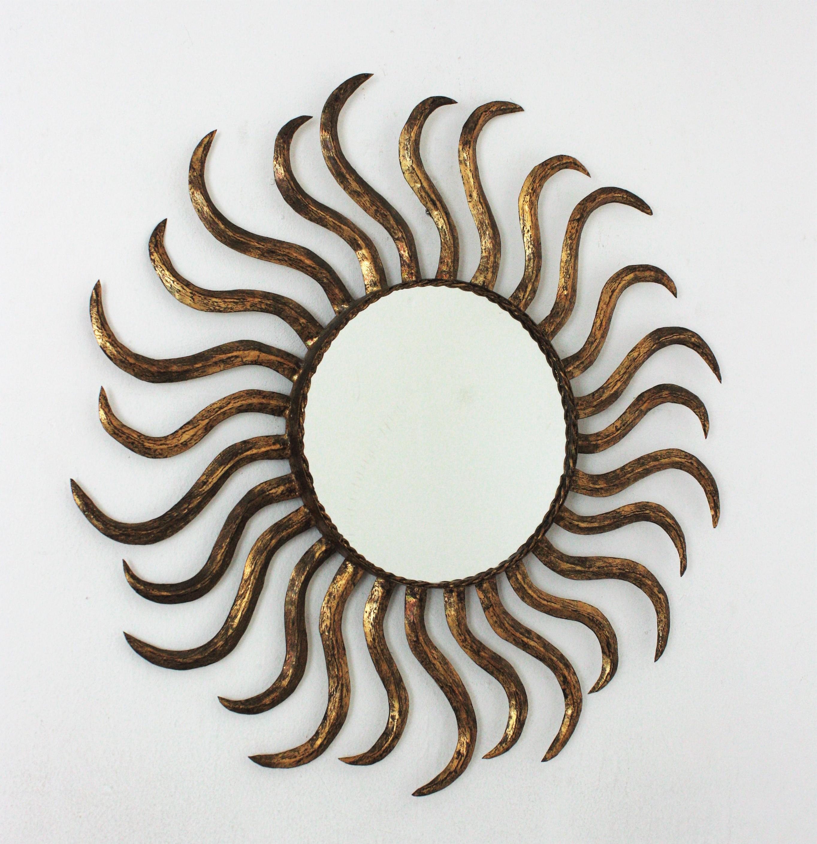 Eye-catching gilt iron sunburst mirror with large rays in pinwheel disposition. France, 1950s.
This wall mirror has a beautiful design and a nice aged patina showing its original gold leaf gilding.
Use it as wall mirror placed alone or as a part