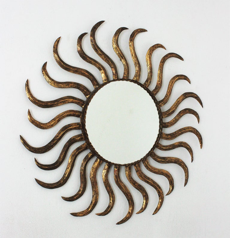 Eye-catching gilt iron sunburst mirror with large rays in pinwheel disposition. France, 1950s.
This wall mirror has a beautiful design and a nice aged patina showing its original gold leaf gilding.
Use it as wall mirror placed alone or as a part