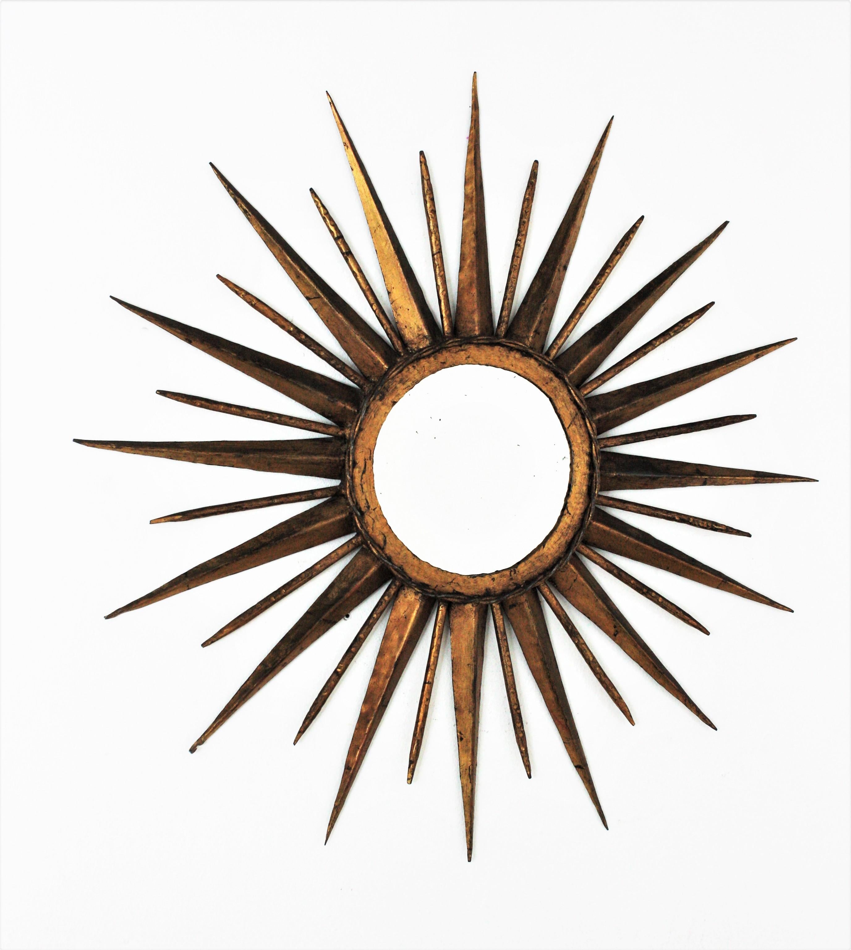 Outstanding hand forged gilt wrought iron large sunburst starburst mirror in the manner of Gilbert Poillerat. France, 1940s.
This wall mirror has an eye-catching starburst design. Entirely made by hand in wrought iron this mirror has a frame